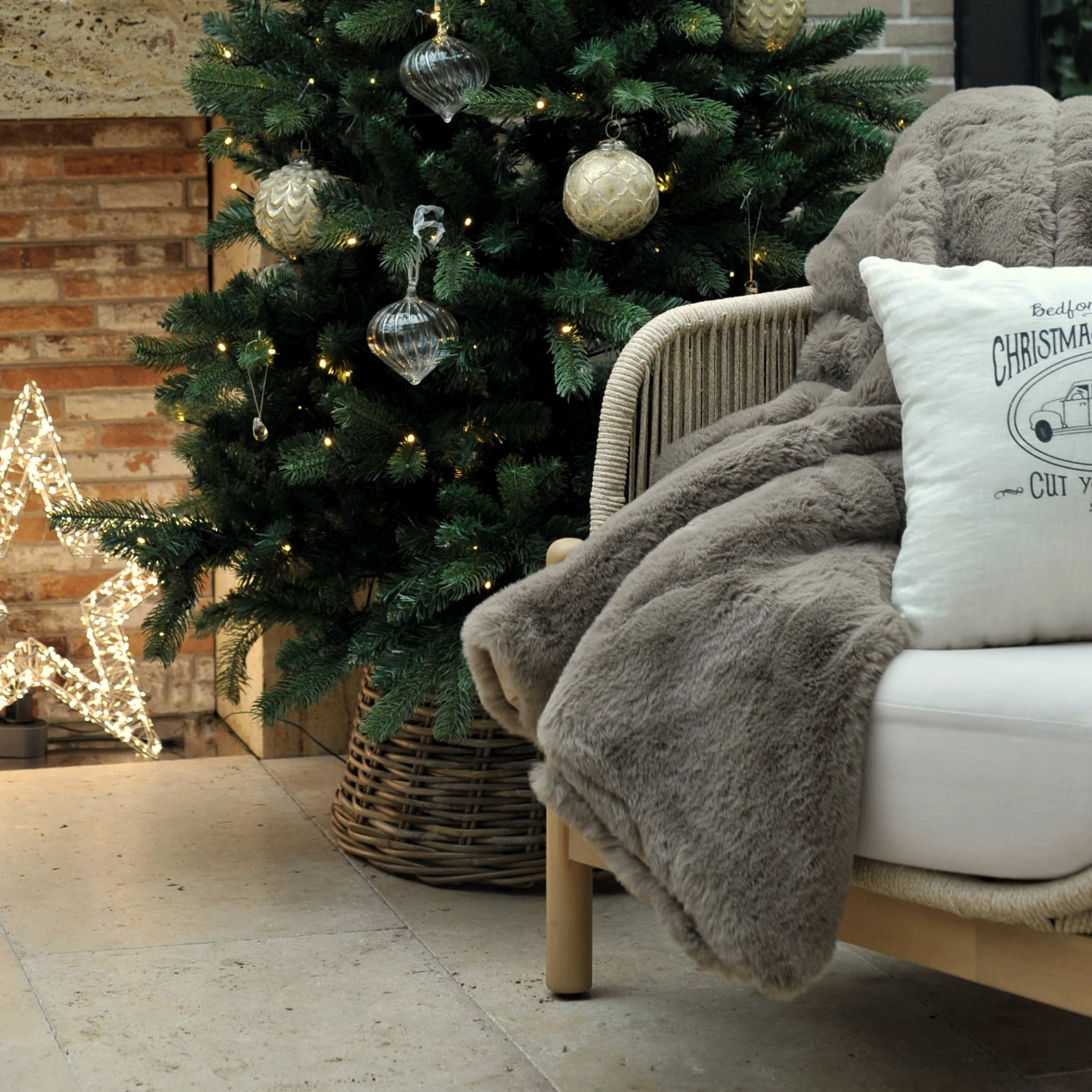 Weiche graue Kunstfelldecke auf Stuhl neben geschmücktem Weihnachtsbaum und leuchtendem Stern