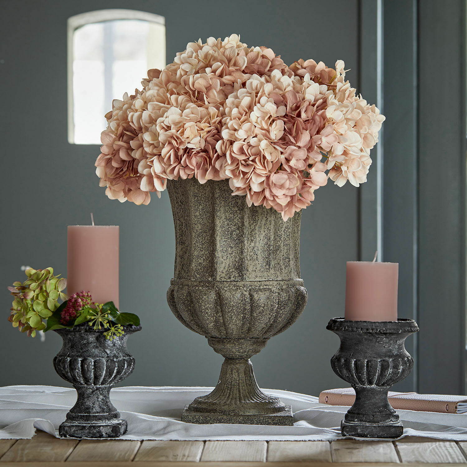 Amphore Renny Dekorativer Steinvase mit rosa Blumen und zwei schwarzen Kerzenhaltern mit rosa Kerzen auf Holztisch