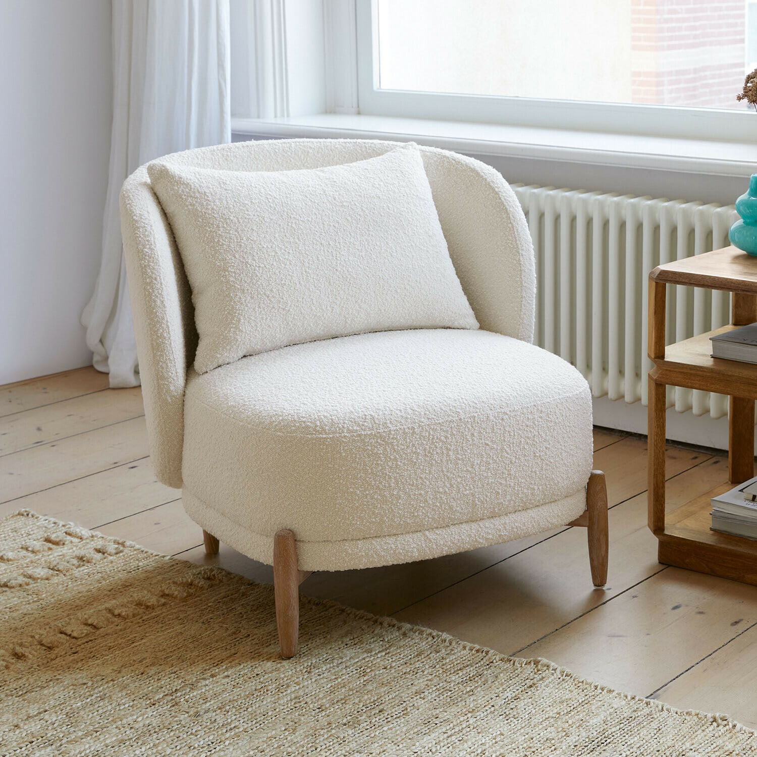 Sessel Thamira Weisser Sessel aus weichem Bouclé-Stoff mit Holzbeinen in hellem Wohnzimmer
