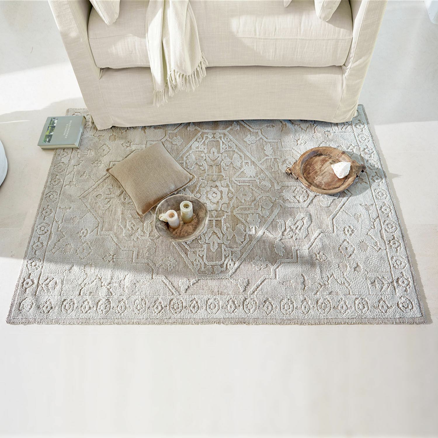 Beiger Teppich mit feinem Muster unter hellem Sofa, Dekokissen und Schalen darauf