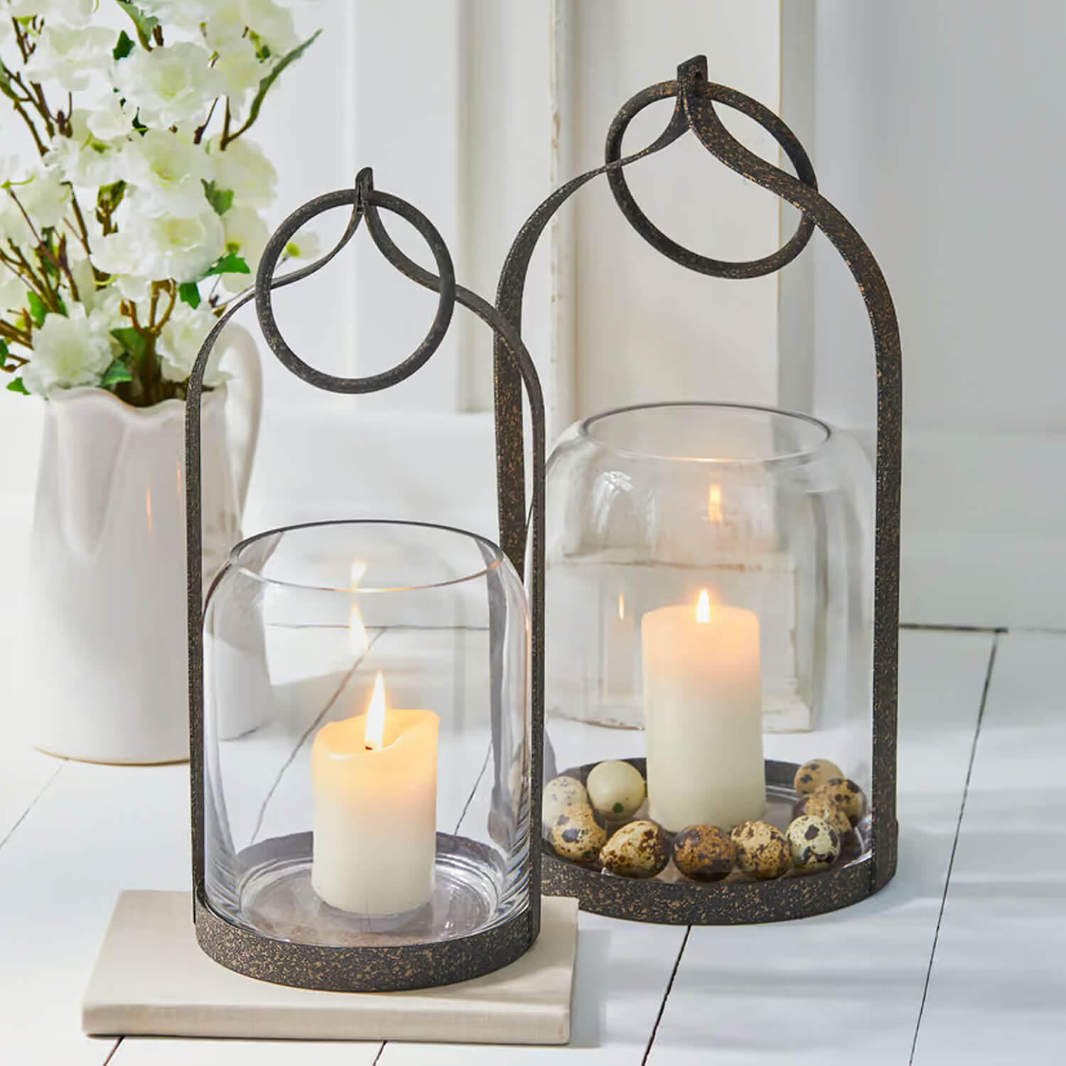 Zwei Metalllaternen mit klarem Glas und weissen Kerzen, dekoriert mit natürlichen Eiern