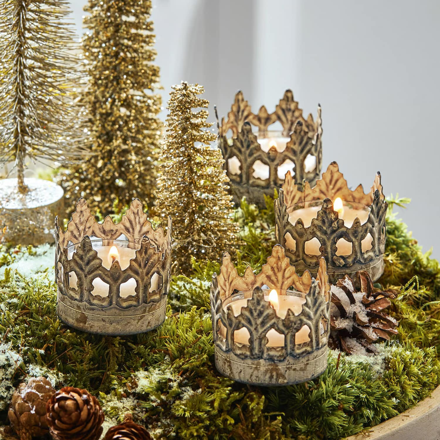 Metall-Kerzenhalter in Kronenform auf grünem Moos mit Weihnachtsdekoration und goldenen Bäumchen