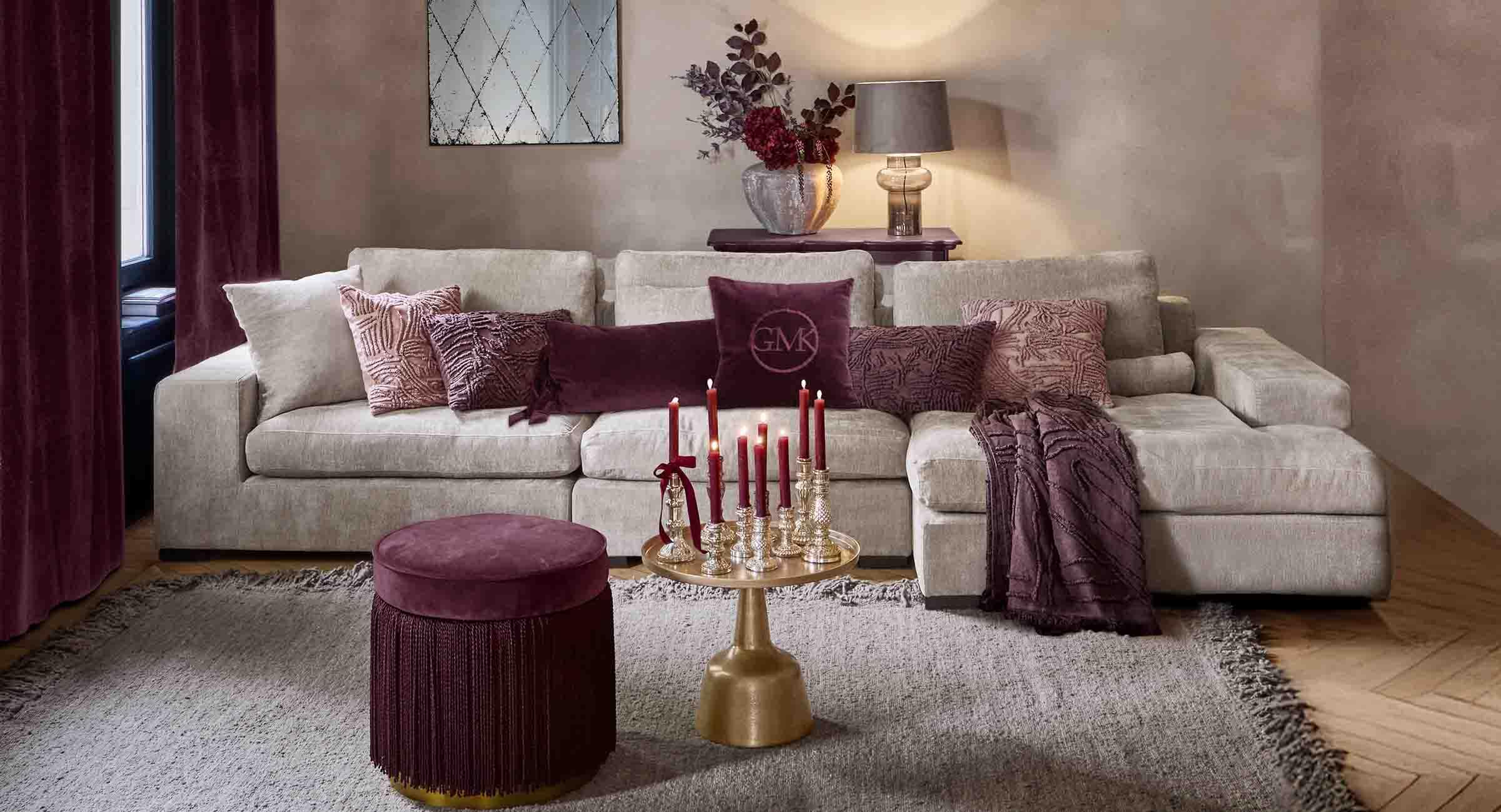 Beige Sofa mit weichen Kissen und bordeauxfarbenen Akzenten in elegantem Wohnzimmer mit Lampe und Spiegel