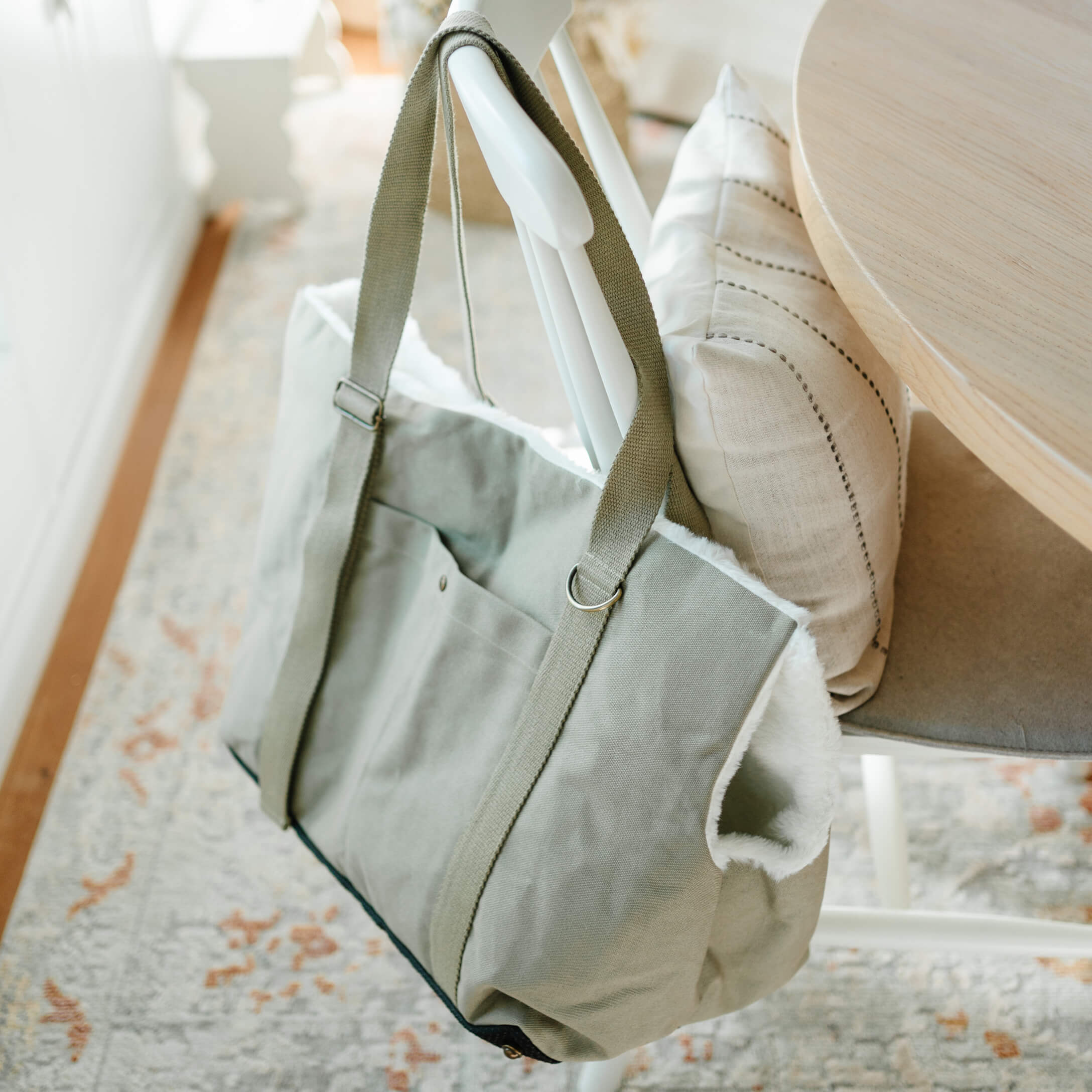Graue Stofftasche mit weissem Fellfutter an weissem Stuhl in hellem Raum