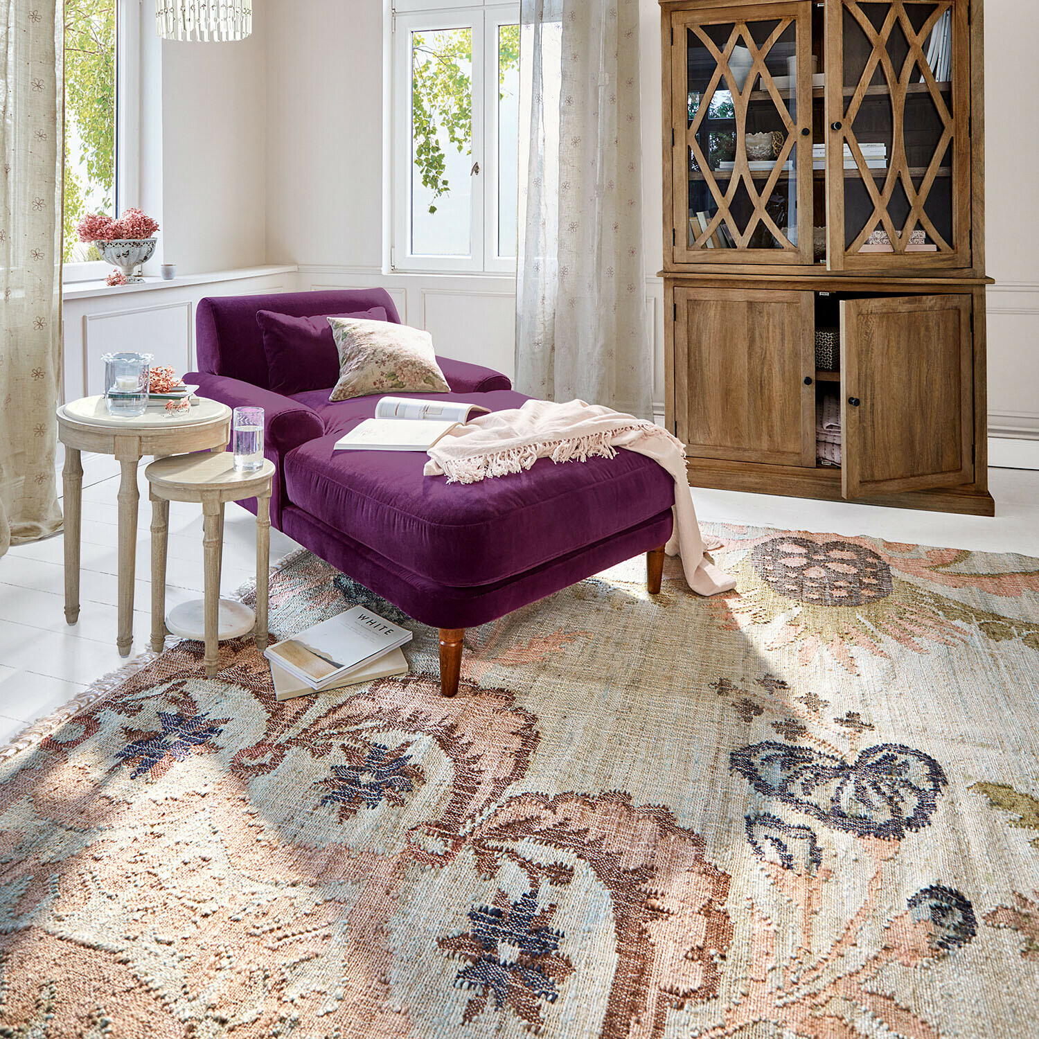 Teppich Amélorie Violette Samt-Chaiselongue in hellem Wohnzimmer mit Holzvitrine und dekorativem Teppich