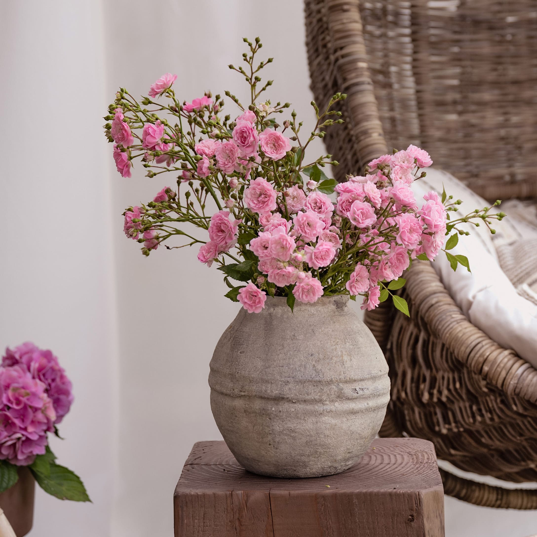 Graue Keramikvase mit rosa Blumen auf Holzblock, stilvolle Wohnraumdekoration
