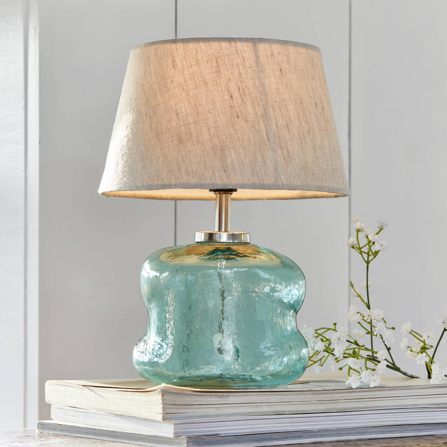 Tischlampe aus blauem Glas mit beigem Lampenschirm auf Bücherstapel, Wohnaccessoire