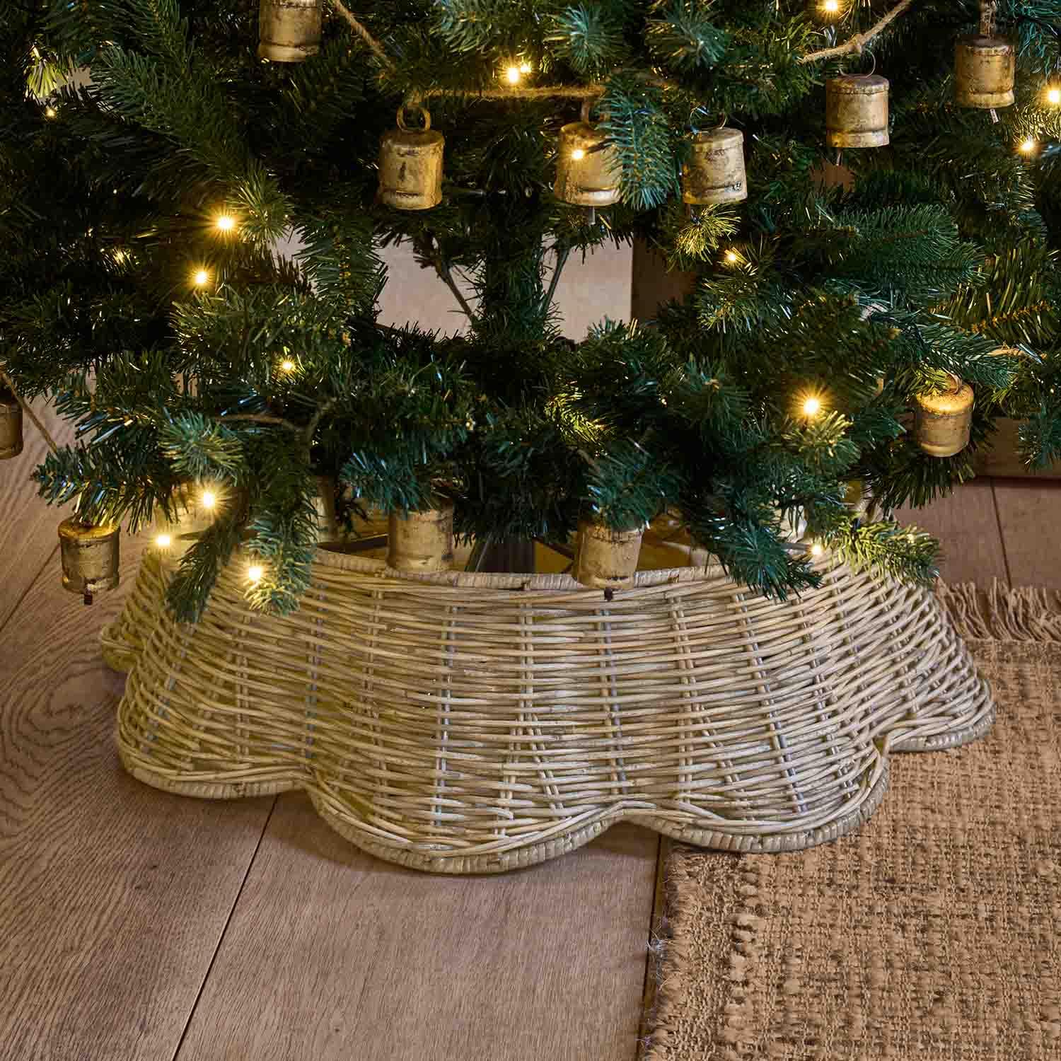 Natürlicher hellbrauner Weidenkorb als Baumständer unter grünem Weihnachtsbaum mit warmen Lichtern
