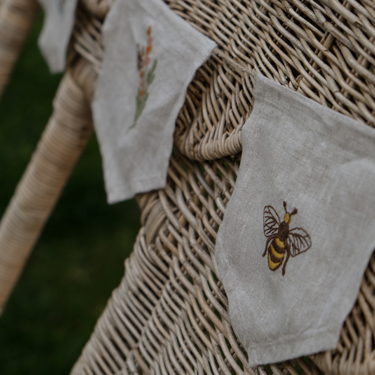 Leinenbeutel mit Bienen- und Blumenstickerei auf natürlichem Rattanstuhl, beige Farbe