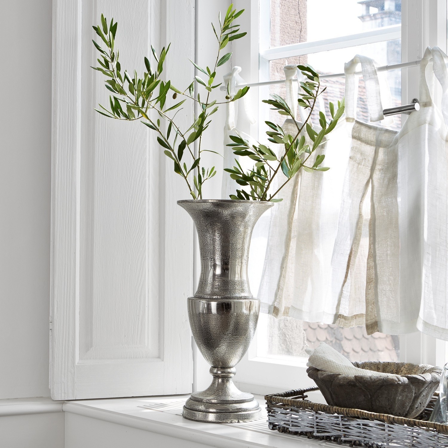 Vase Gilberta Silberne Metallvase auf der Fensterbank mit grünen Zweigen und natürlichem Licht