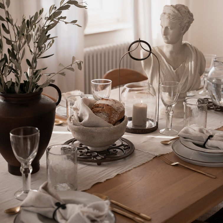 Rustikaler Tisch mit steinerner Brotschale, Kerze unter Glasglocke und weisser Steinskulptur als Dekor