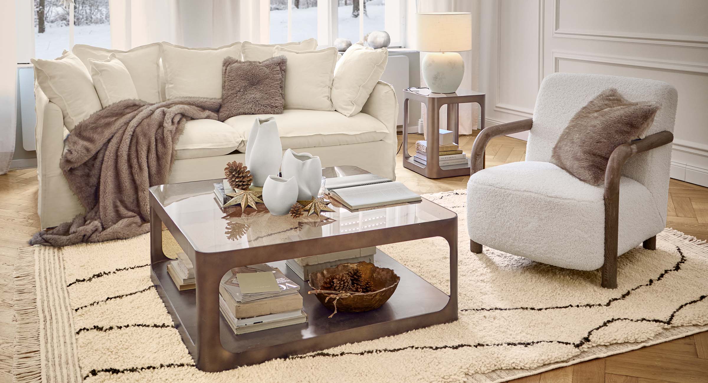 Gemütliches Wohnzimmer mit weissem Sofa, Sessel und brauner Decke auf gemustertem Teppich