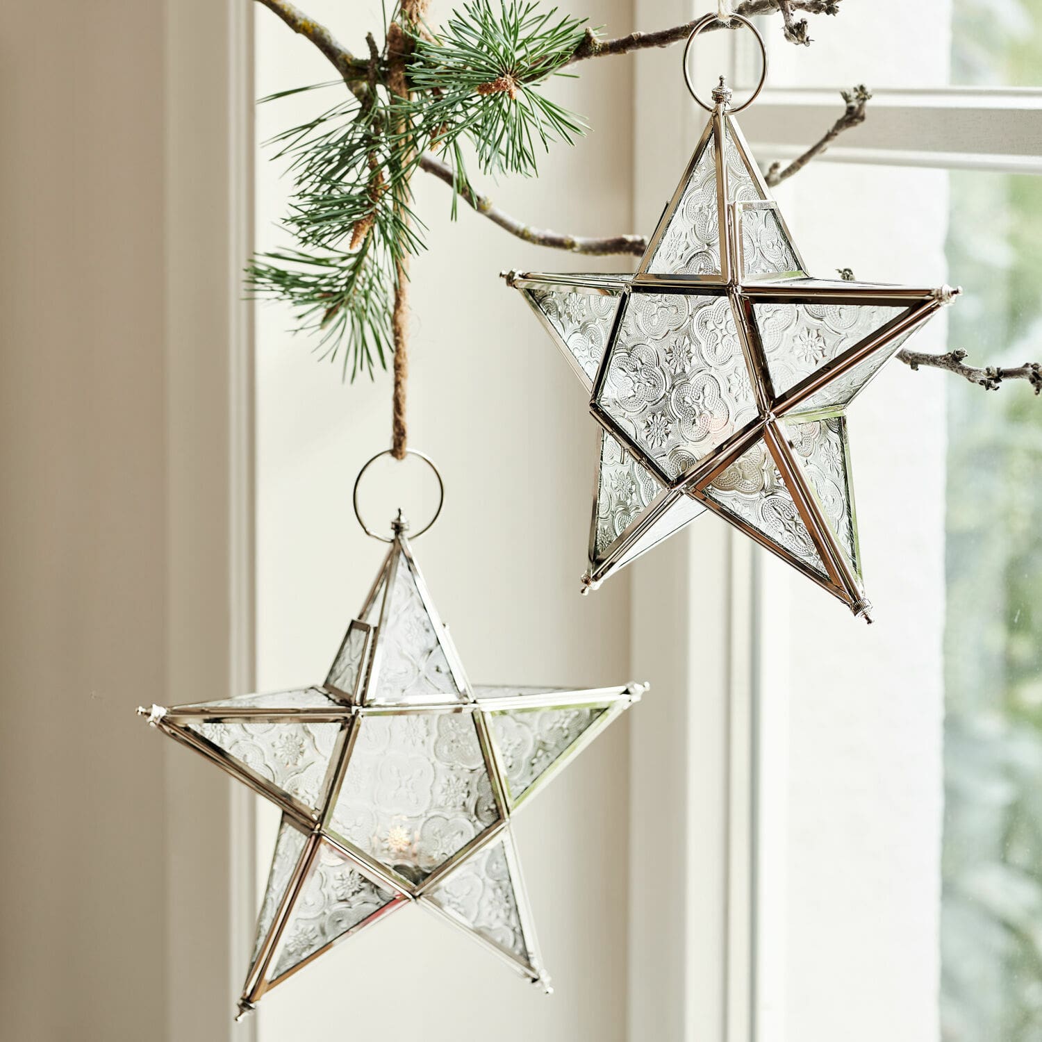 Glassterne mit silbernem Metallrahmen, an einem Kiefernzweig hängend, Weihnachtsdekoration