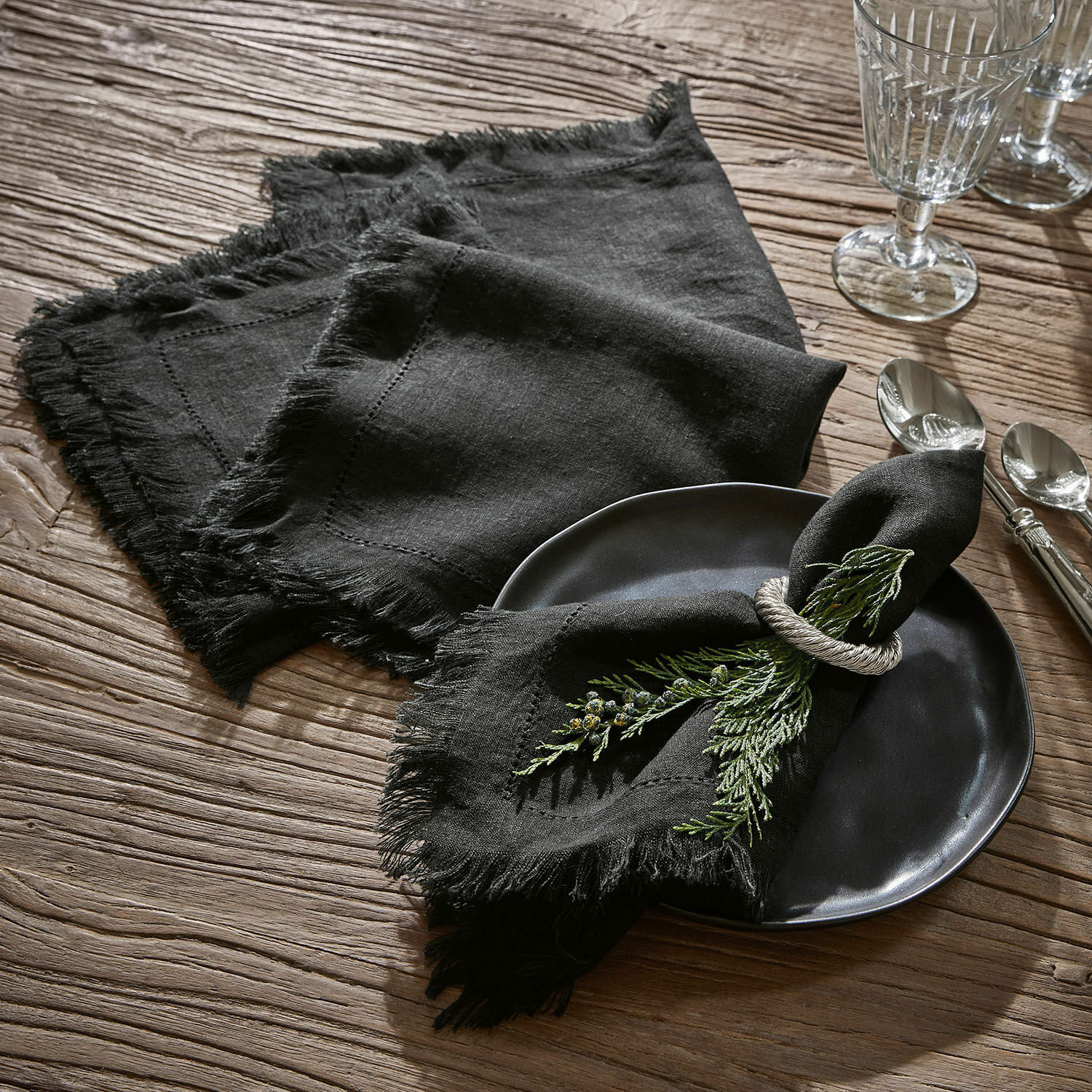 Serviette 4er Set Pibrac Schwarze Leinenservietten mit Fransen auf Holztisch mit grüner Zweigdekoration