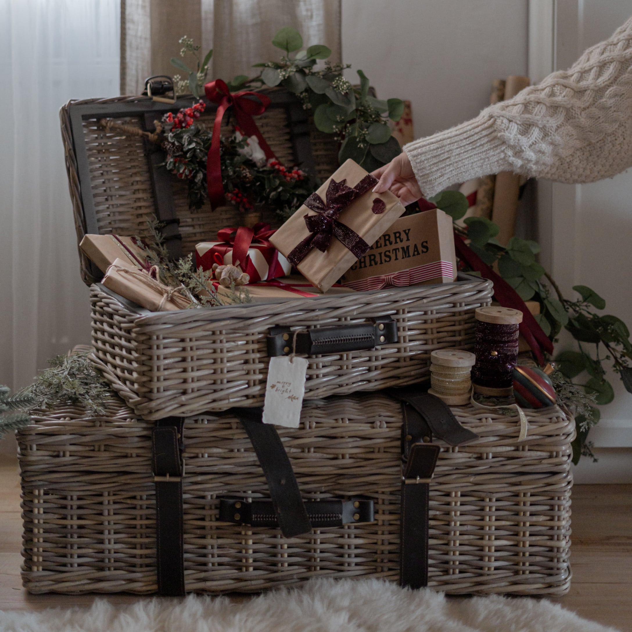 Zwei graue Rattankörbe mit dunklen Lederriemen, geschmückt mit Weihnachtsgeschenken und Dekorationen.