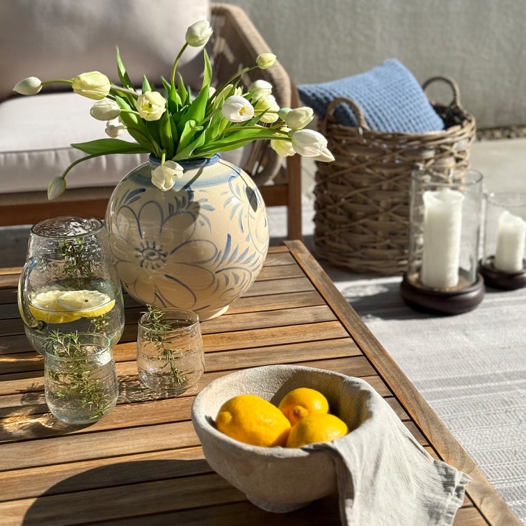 Dekorativer Keramikvase mit Blumenmuster und weissen Tulpen auf Holztisch auf der Terrasse