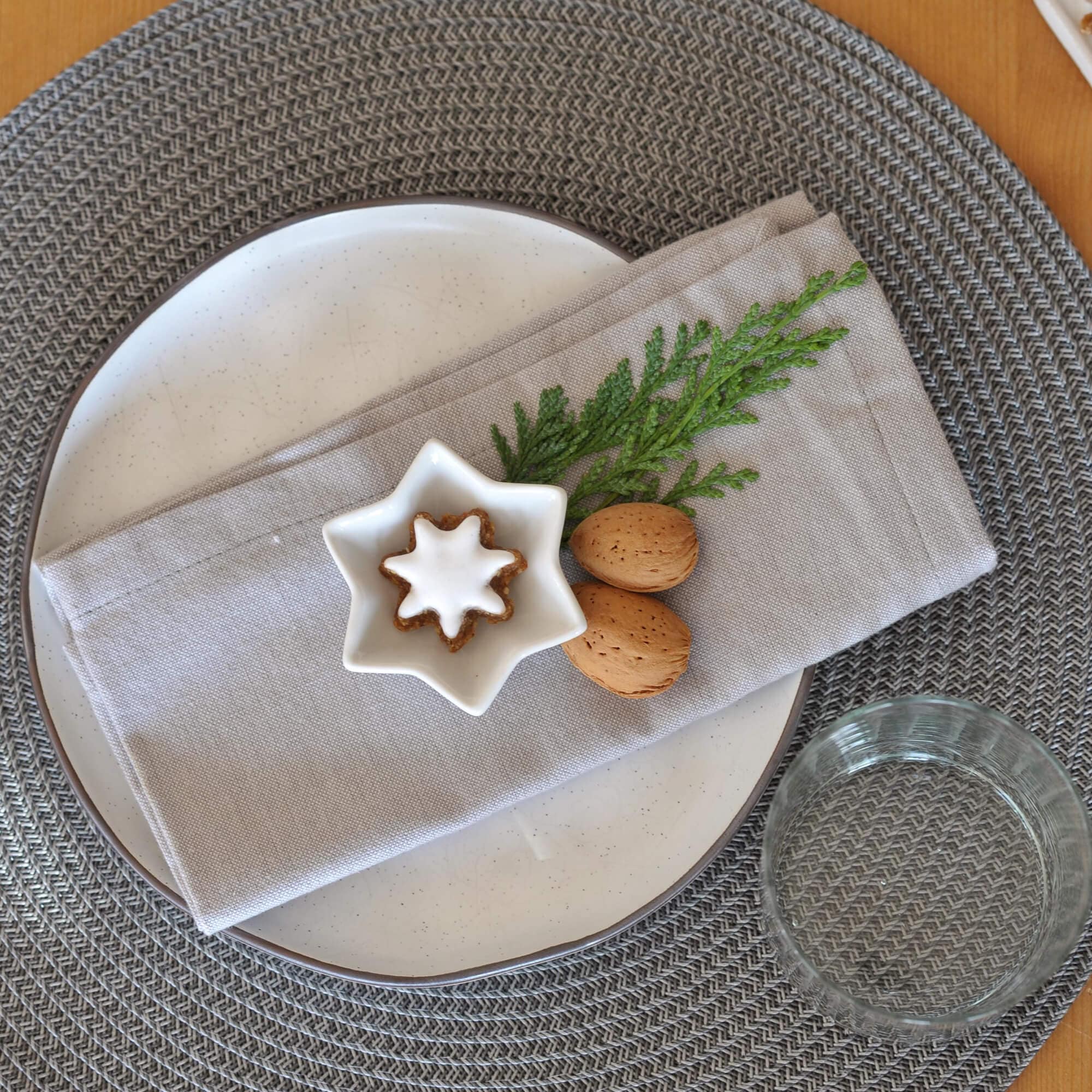 Graue geflochtene Tischunterlage mit weissem Teller, Leinenserviette und Weihnachtsdekoration
