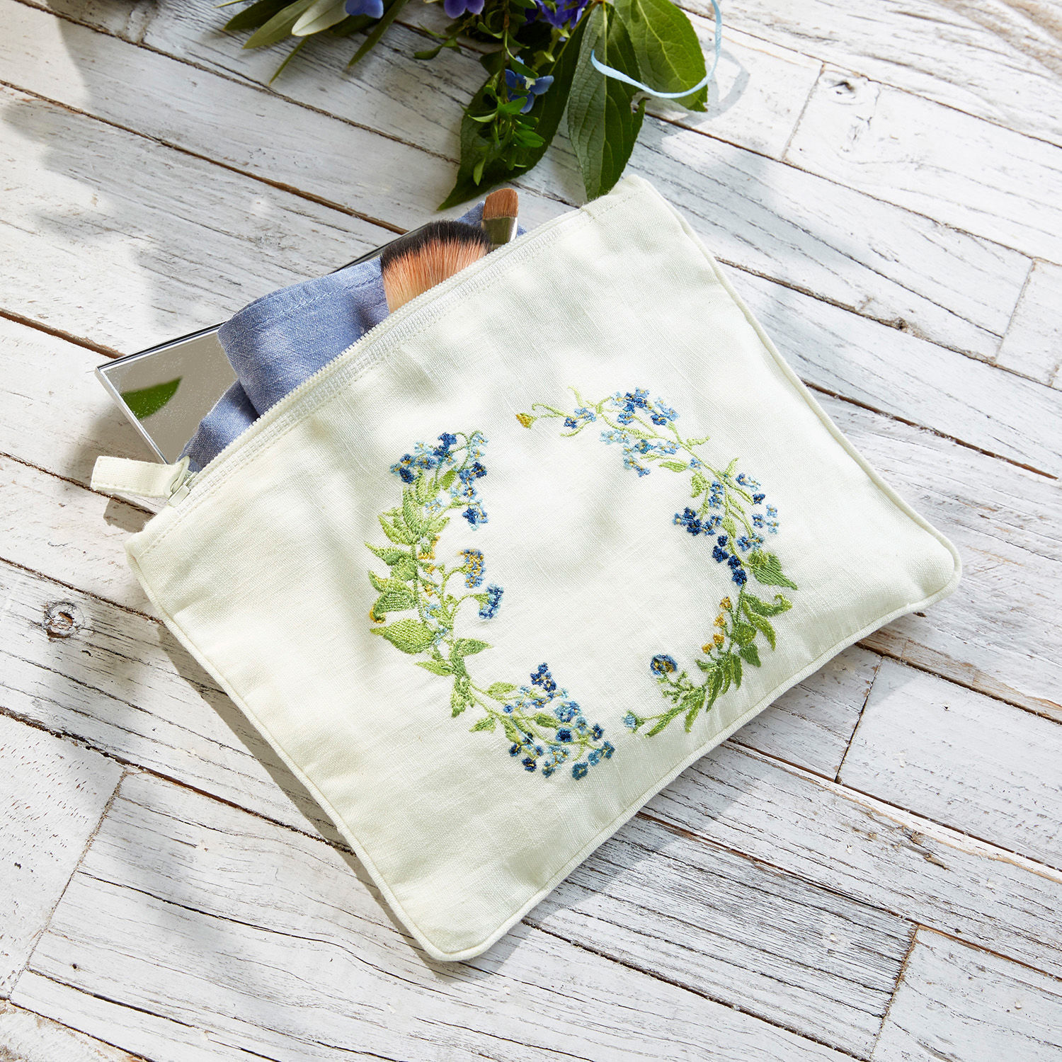 Täschchen Fierolla Weisse Kosmetiktasche aus Leinen mit blauer Blumenstickerei auf hellem Holzhintergrund