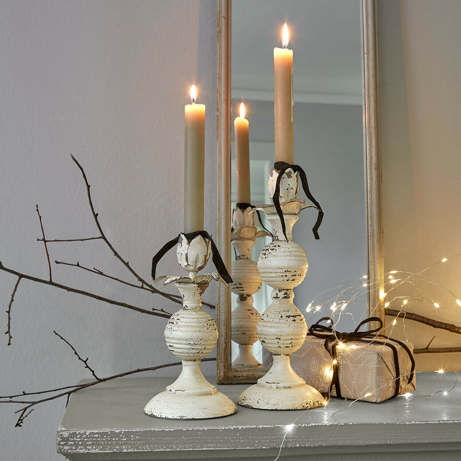 Kerzenhalter 2er Set Soliras Zwei cremefarbene Metall-Kerzenhalter mit beigen Kerzen und schwarzem Band auf grauem Regal mit Lichterkette