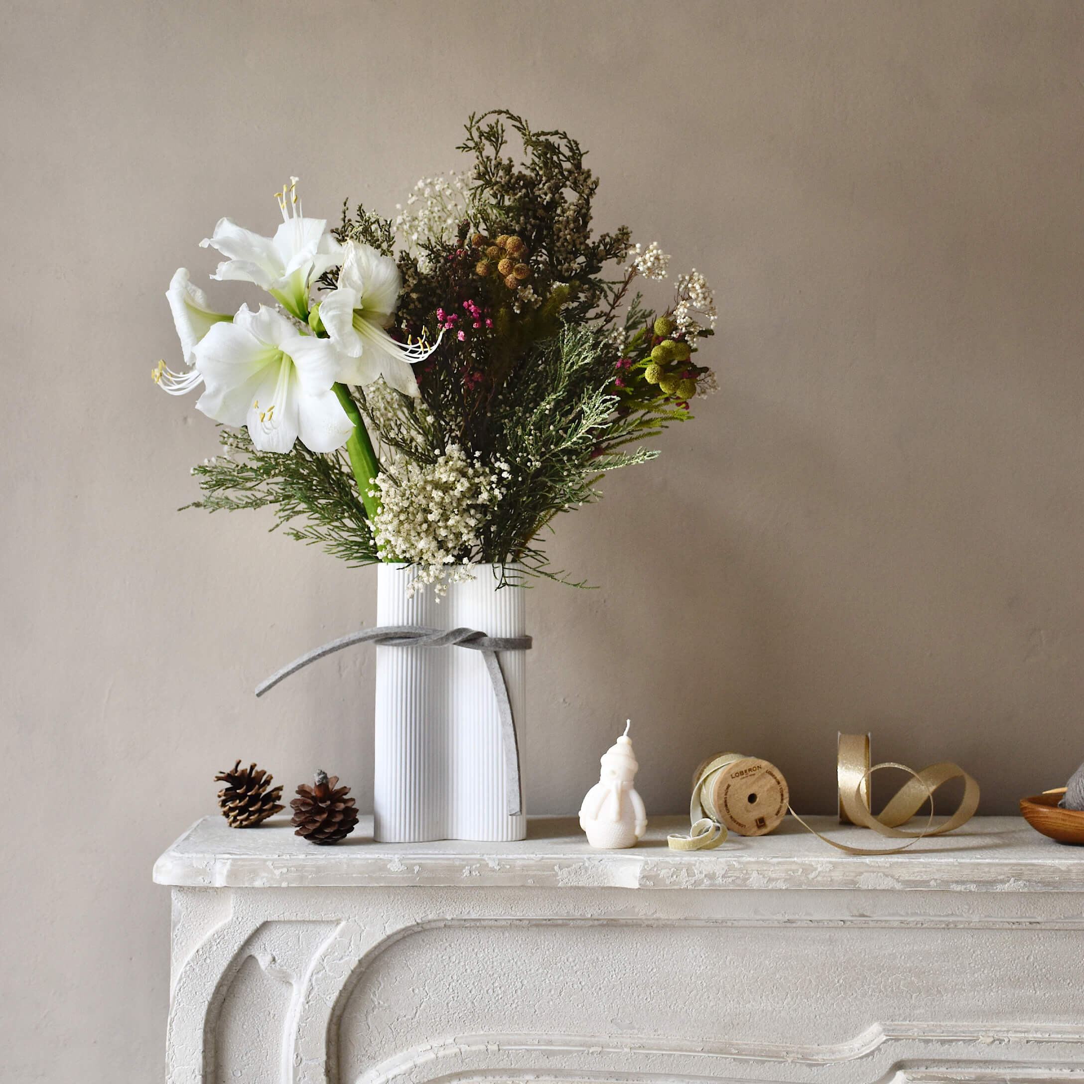 Weisse Keramikvase mit weissen Blumen und grünen Zweigen auf einem dekorativen weissen Kamin
