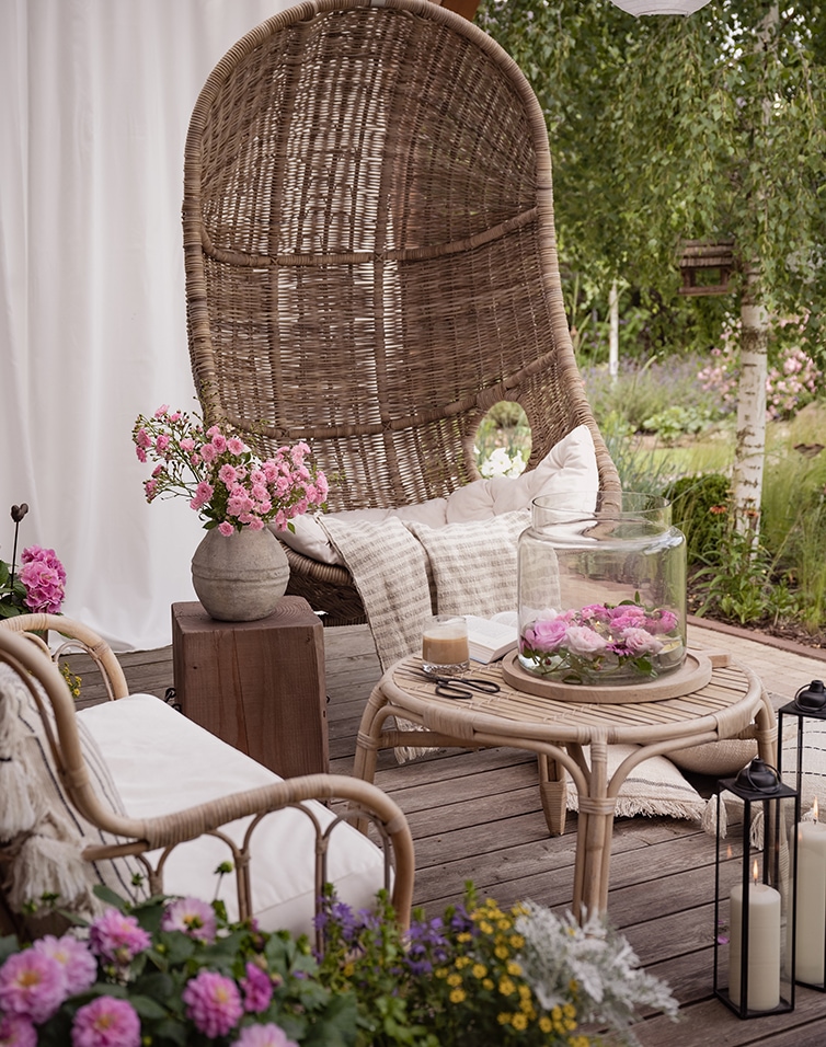 Garten mit Rattansessel und Beistelltisch aus Naturmaterial, dekoriert mit Blumen auf Holzterrasse