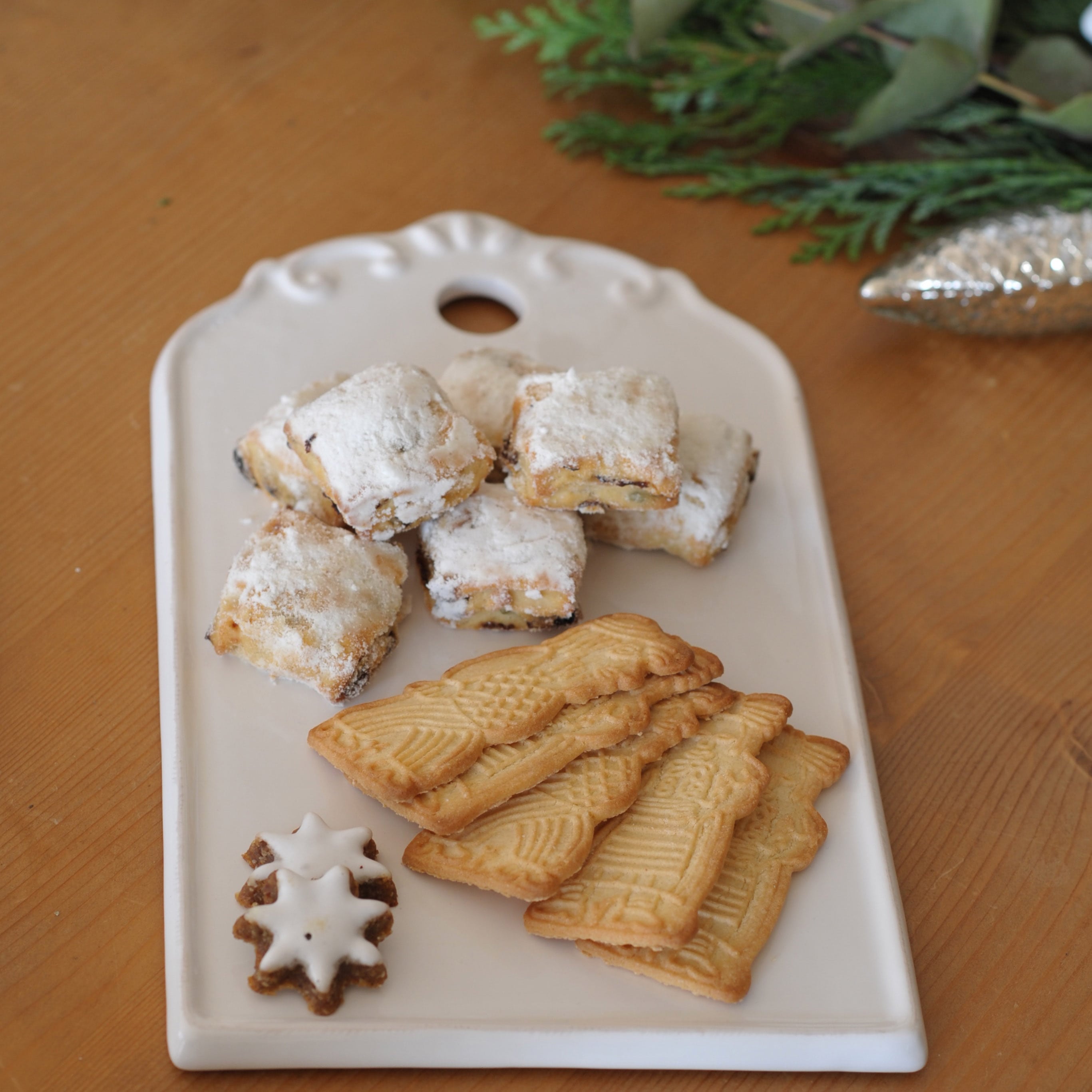 Weisses Keramiktablett mit traditionellen Weihnachtsguetzli auf Holztisch