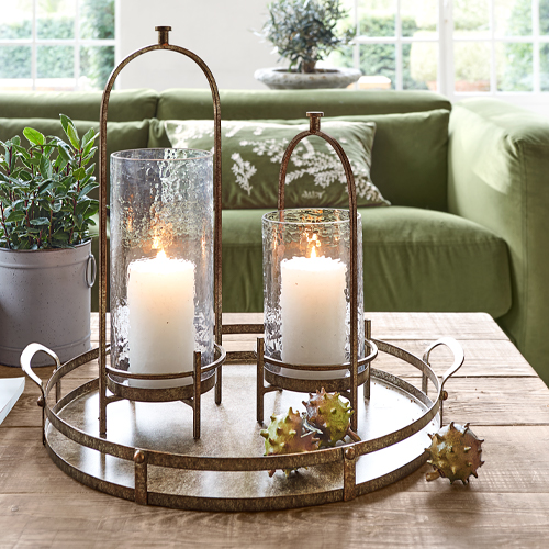 Metalltablett mit zwei Glaslaternen und weissen Kerzen auf hellem Holztisch im Wohnzimmer