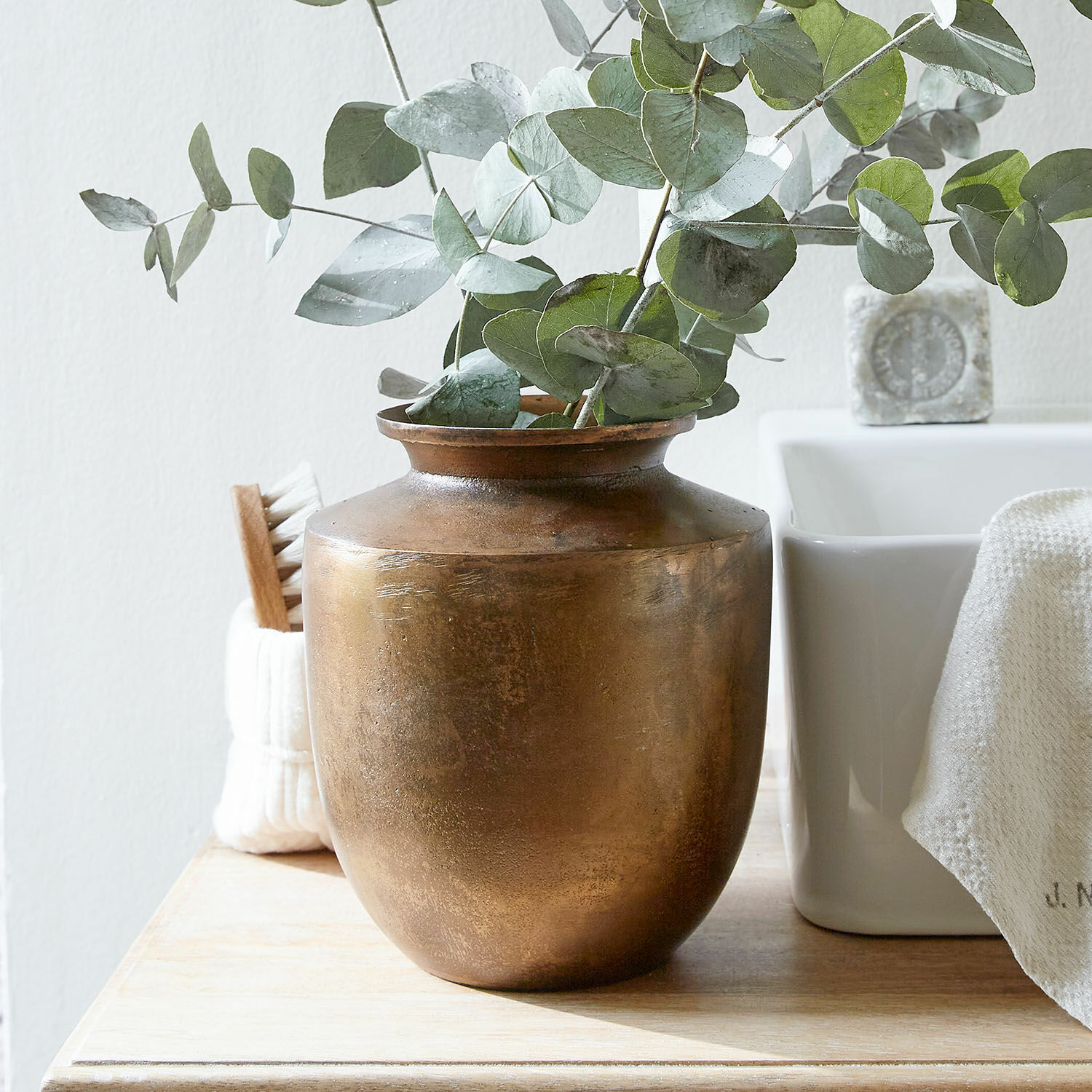 Vase Toulane Messingvase mit grünen Eukalyptusblättern auf Holzplatte in hellem Raum
