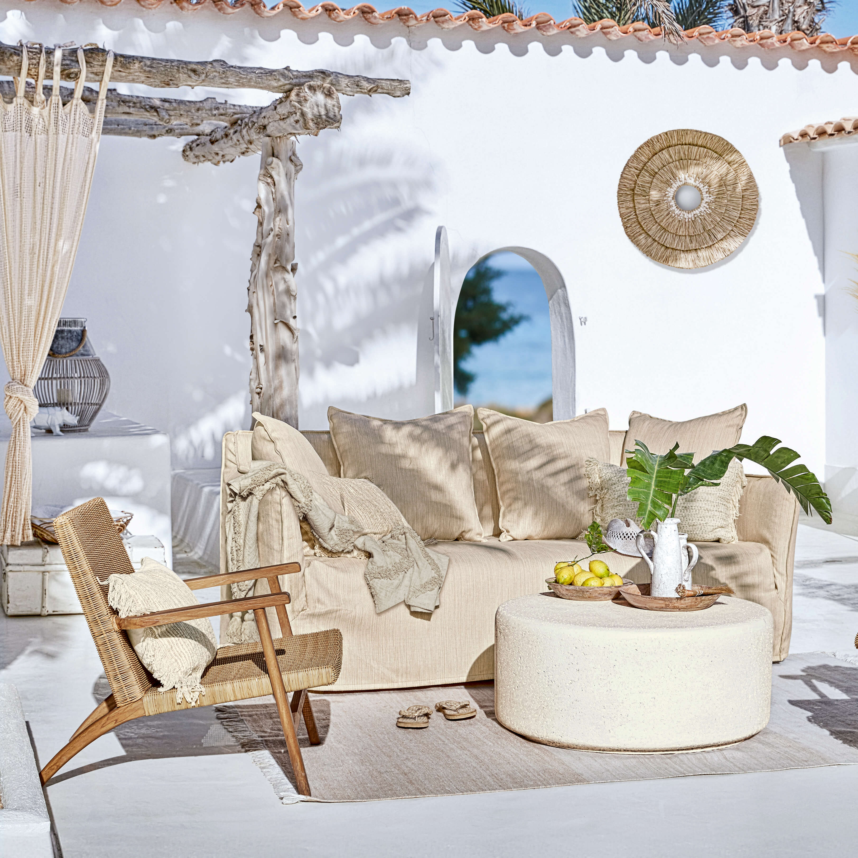 Beiges Sofa und Rattansessel auf der Terrasse mit natürlichen Dekorationen und rundem Couchtisch