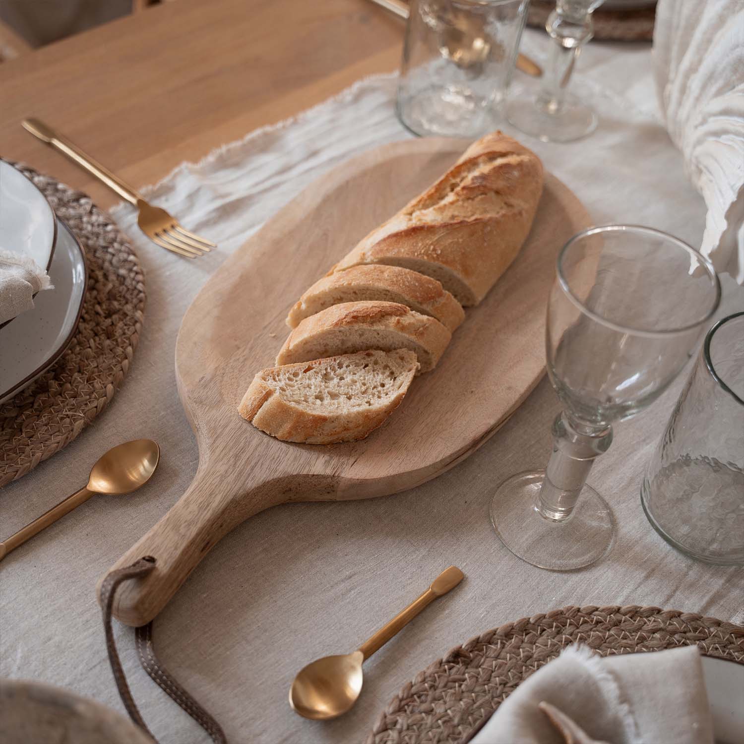 Holzbrett mit geschnittener Baguette auf Tisch mit natürlichem Leinentuch und goldfarbenem Besteck