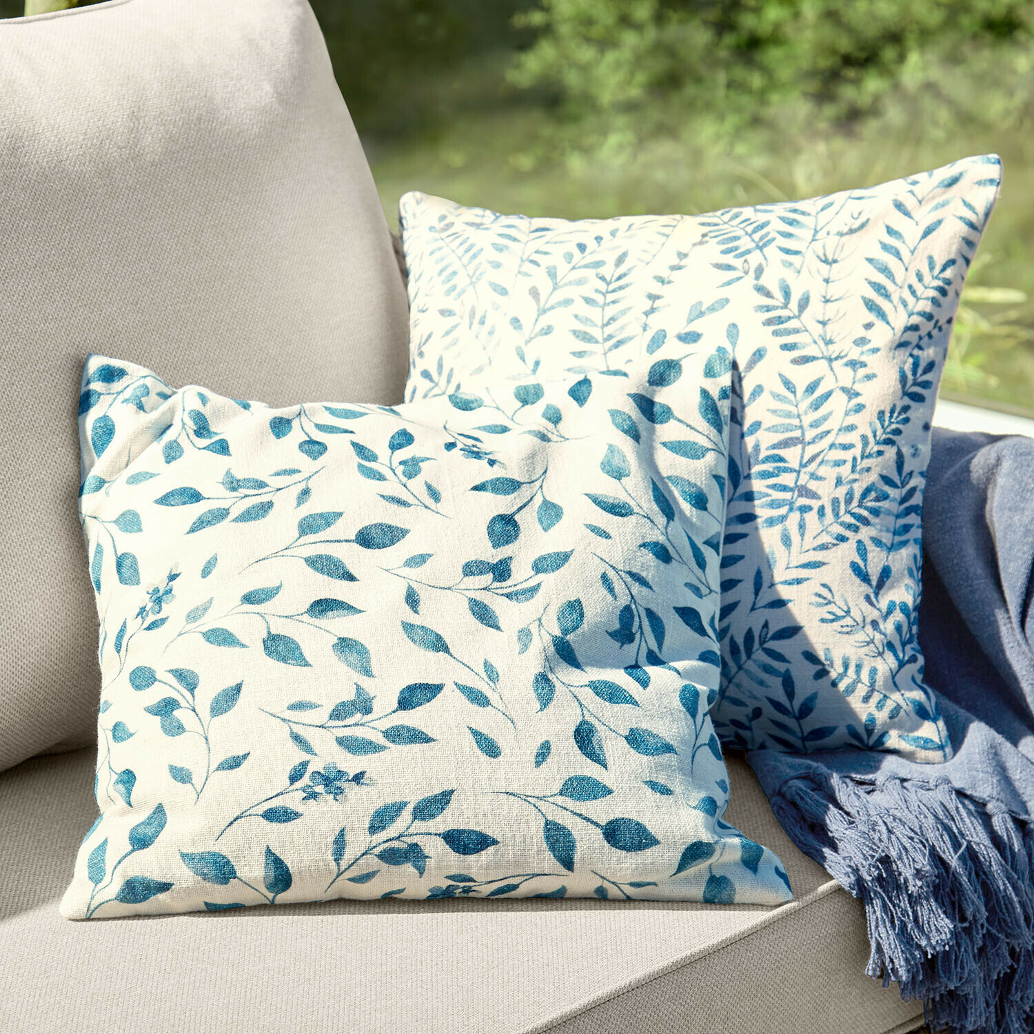 Zwei dekorative Baumwollkissen in Creme mit blauem Blattmuster auf beigem Sofa