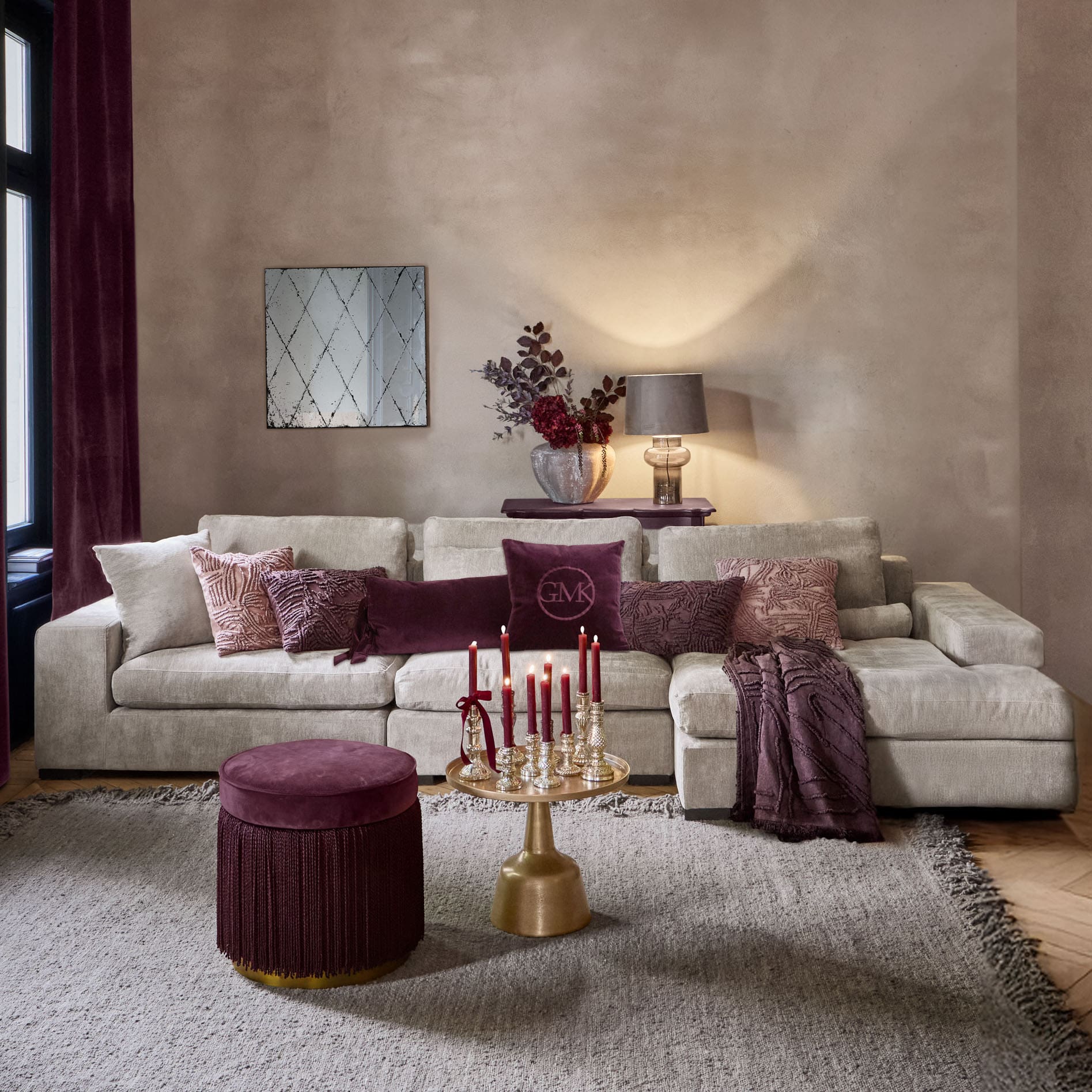 Gemütliches Wohnzimmer mit beigem Sofa, bordeauxfarbenen Kissen und goldenem Tisch mit roten Kerzen