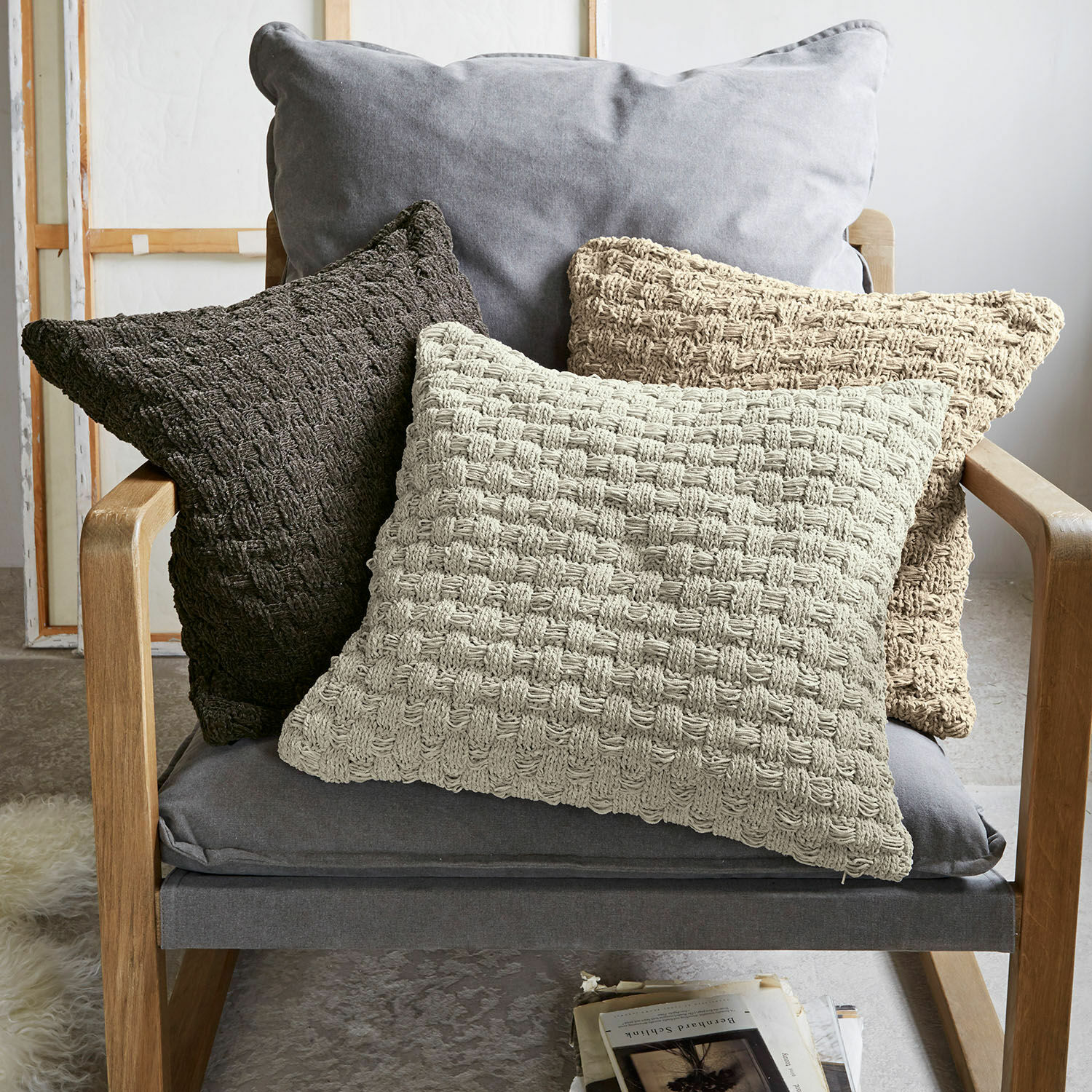 Kissenhülle 3er Set Antier Drei dekorative Kissen aus gewebtem Material in Beige- und Brauntönen auf grauem Sessel.