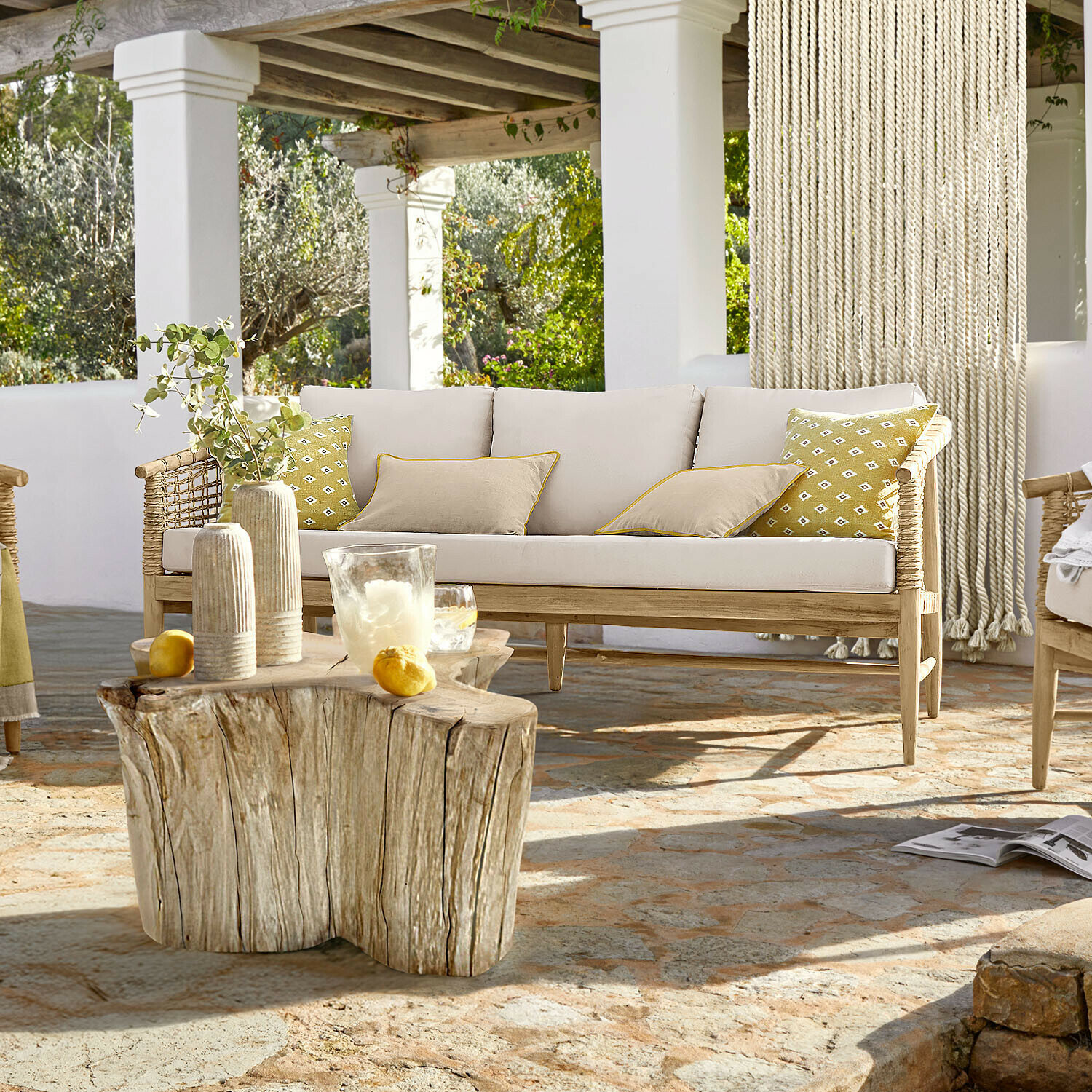 Sofa Roselva Sofa aus hellem Holz mit beigen Kissen und gelben Akzenten auf Terrasse mit Natursteinboden