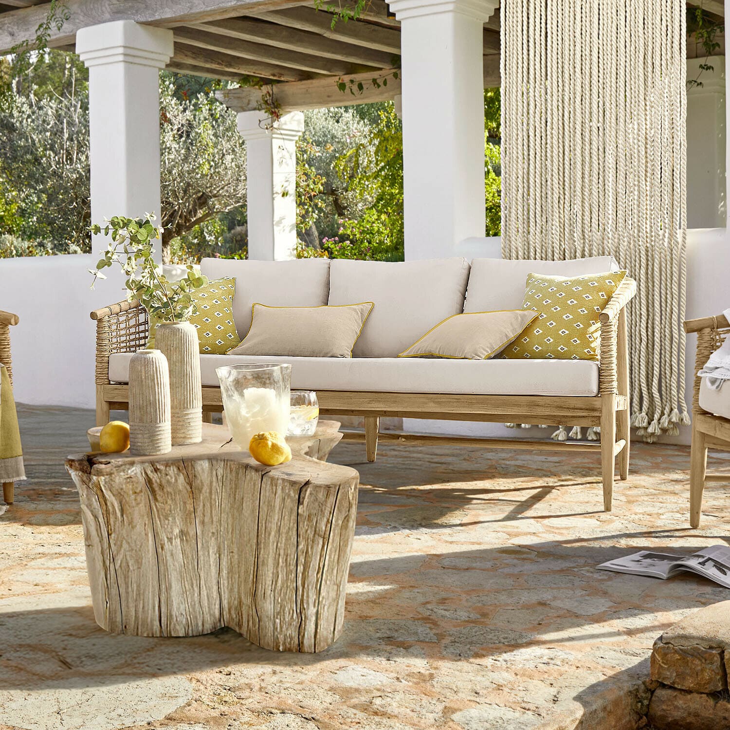 Sofa Roselva Sofa aus hellem Holz mit beigen Kissen und gelben Akzenten auf Terrasse mit Natursteinboden