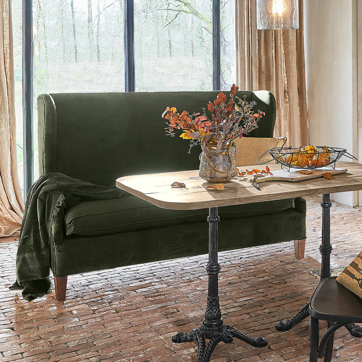 Sofa Ombra Grünes Samtsofa neben Holztisch mit Metallbeinen in hellem Raum mit Ziegelboden.