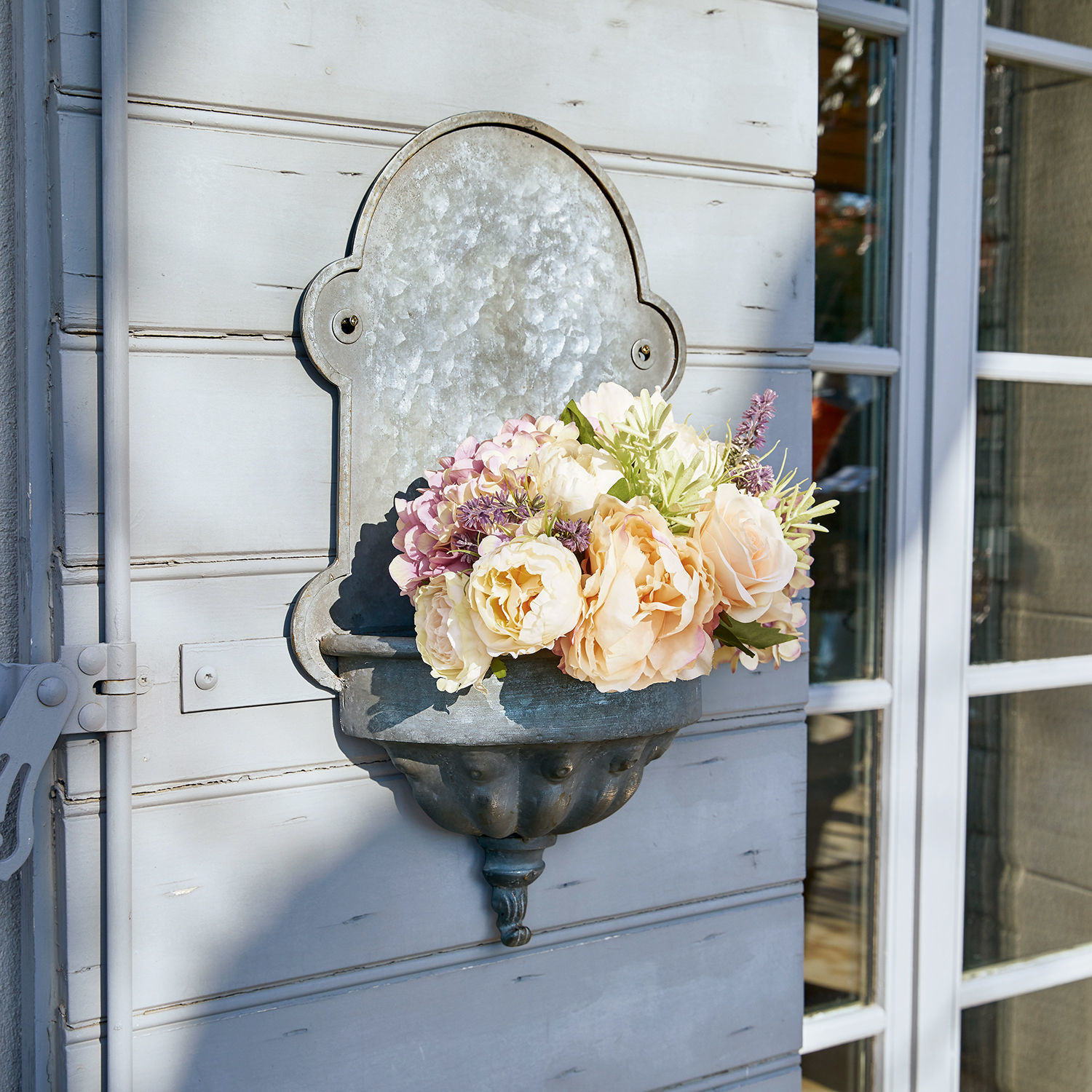 Pflanzbrunnen Millieur Metall-Wandblumenkasten mit pastellfarbenen Blumen an hellgrauer Aussenwand