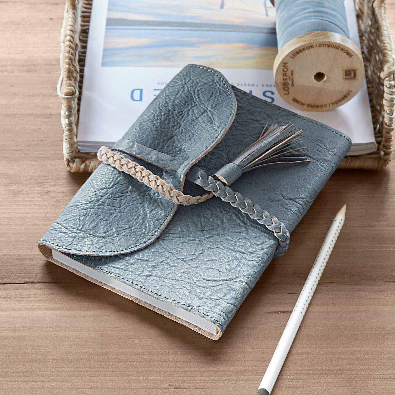 Graues Leder-Notizbuch mit geflochtenem Verschluss und Quaste auf Holztisch mit Bleistift