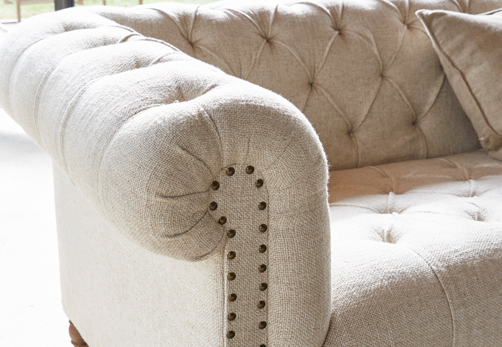Beiges klassisches Sofa aus Stoff mit gesteppter Rückenlehne und dekorativen Nägeln im Wohnzimmer
