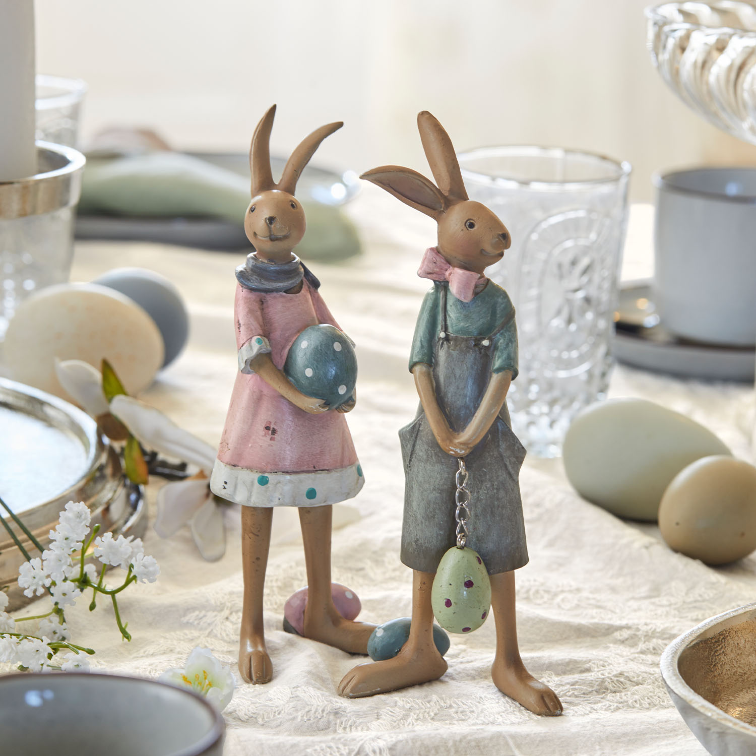 Zwei dekorative Keramik-Hasenfiguren in Pastellfarben mit Ostereiern auf einem Tisch