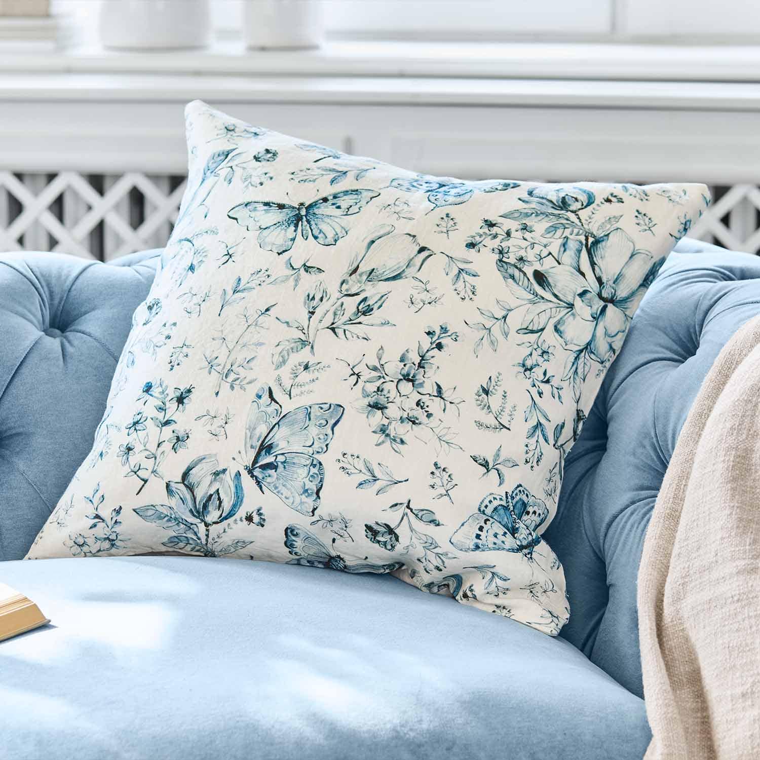 Dekoratives Baumwollkissen mit blauem Schmetterlings- und Blumenmuster auf hellem Hintergrund auf blauem Sofa