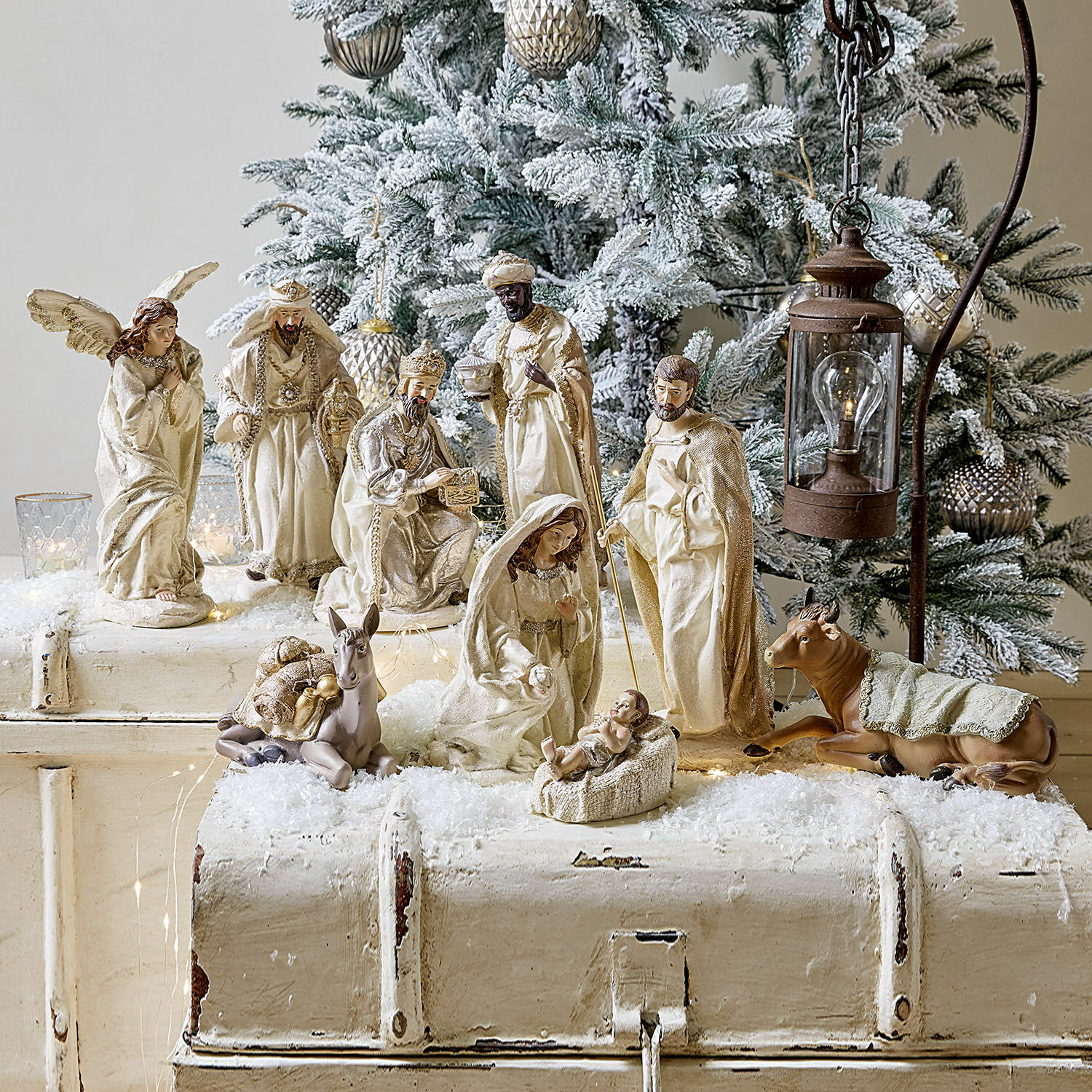 Figur 9er Set Liré Krippenfiguren in Cremefarben vor schneebedecktem Weihnachtsbaum und rustikalem Laternenlicht