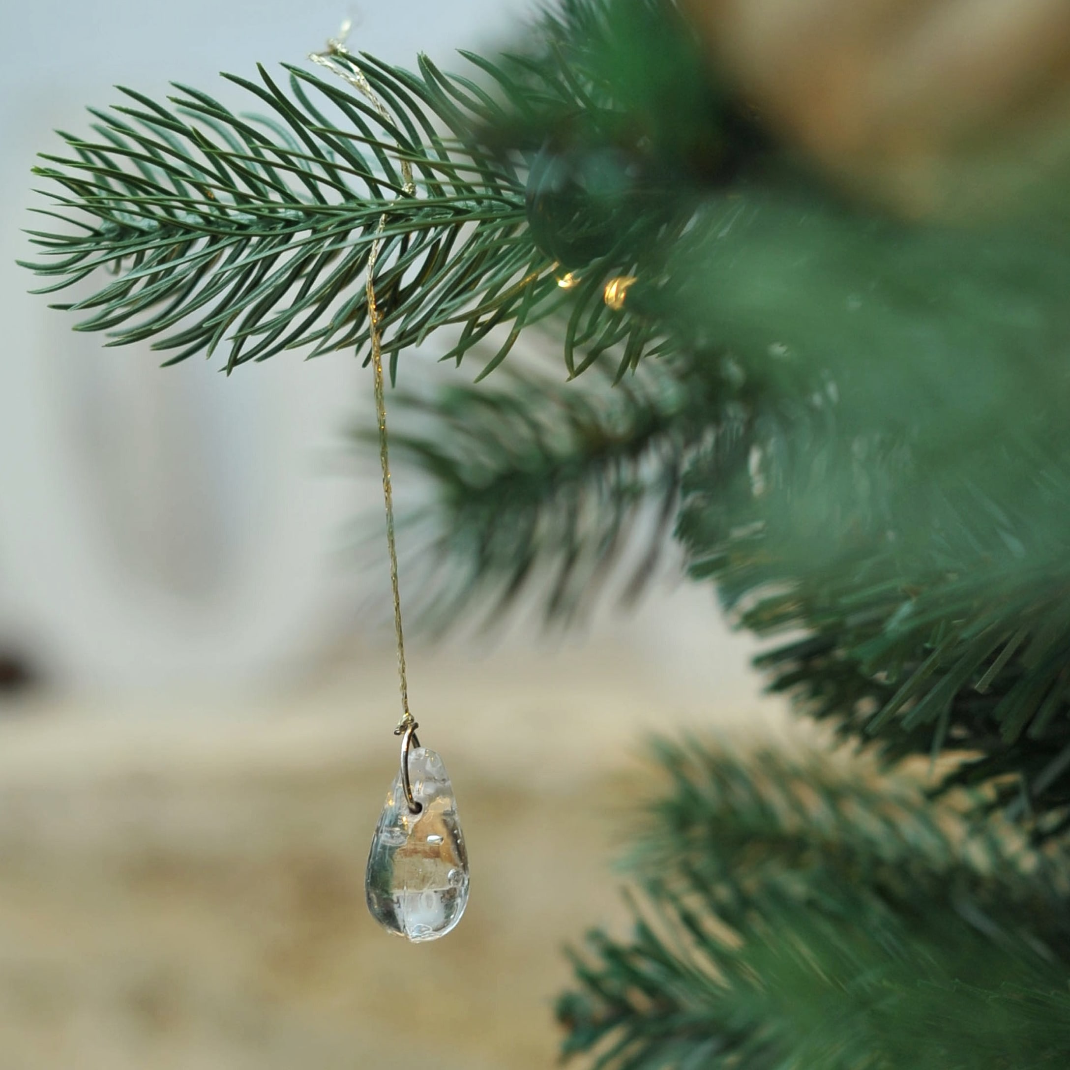Transparenter Glasanhänger an grünem Tannenzweig im hellen Wintergarten-Dekor