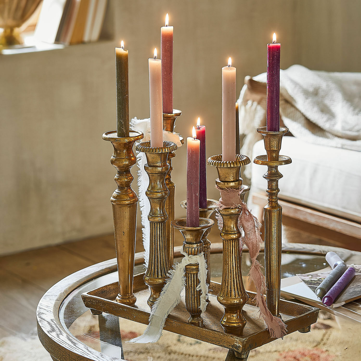 Kerzentablett Chavelot Set aus goldfarbenen Metallkerzenhaltern mit bunten brennenden Kerzen auf Glastisch.