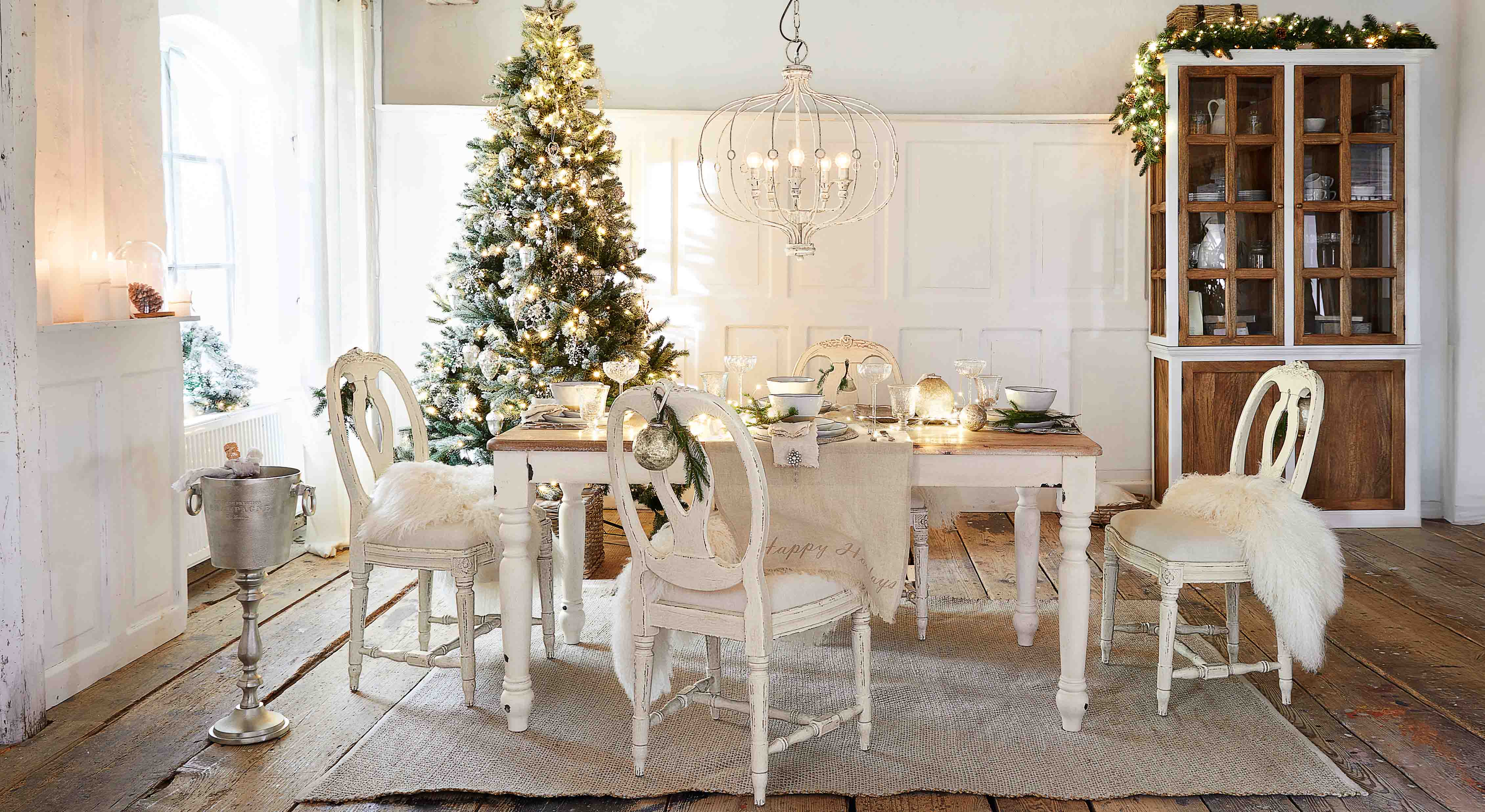 Esszimmer mit weissem Holztisch und Stühlen, festlich dekoriert mit Weihnachtsbaum und Lichterketten