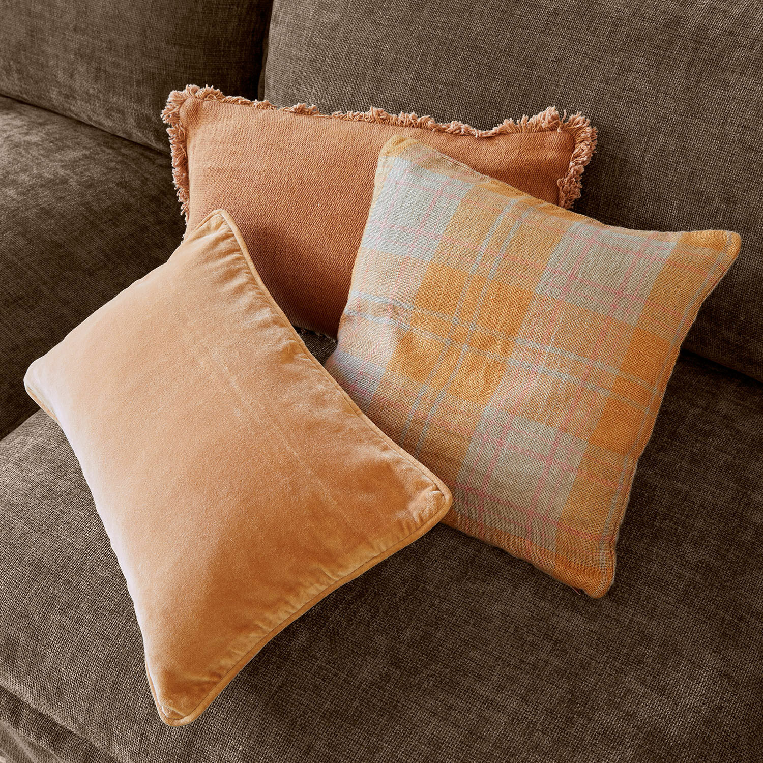 Kissenhülle 3er Set Léonille Drei dekorative Kissen in Orangetönen auf braunem Sofa für ein gemütliches Wohnzimmer