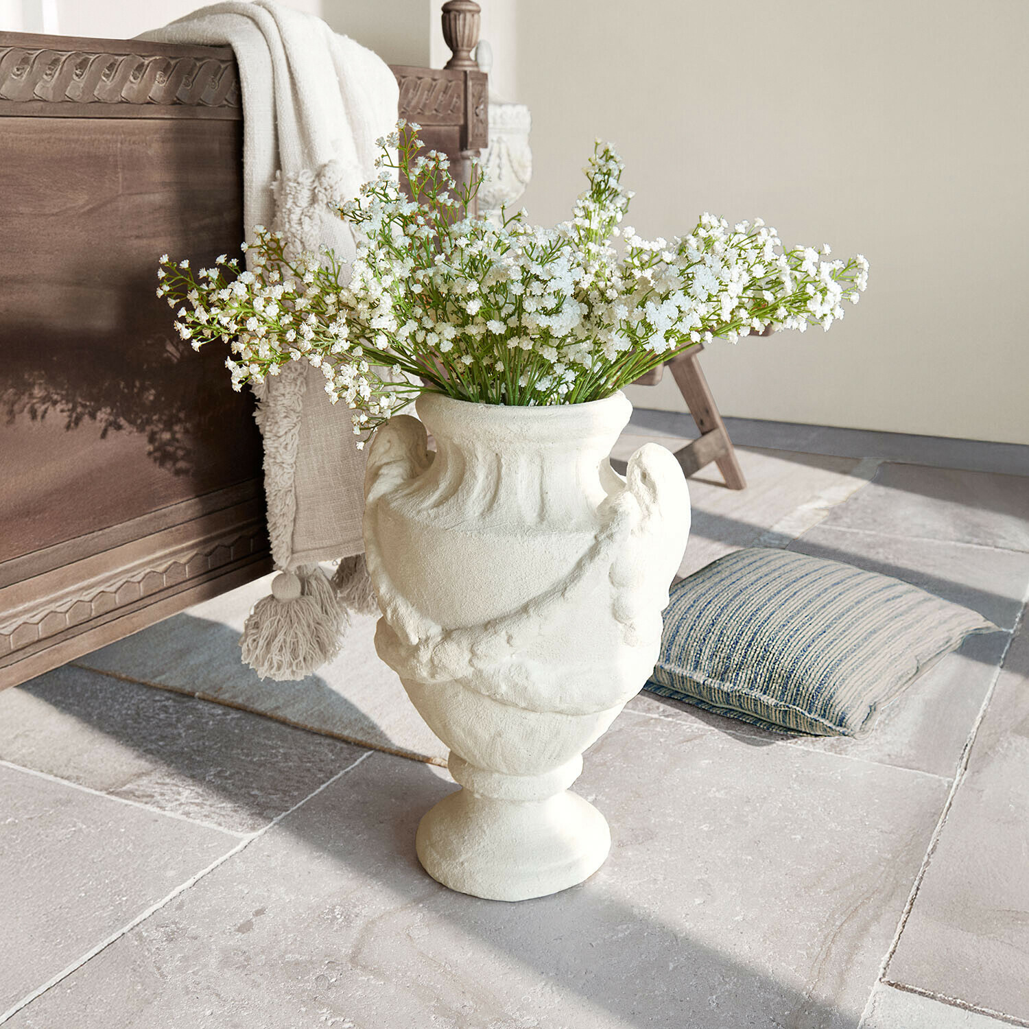 Weisse Keramikvase mit dekorativem Muster und weissen Blumen auf Steinboden