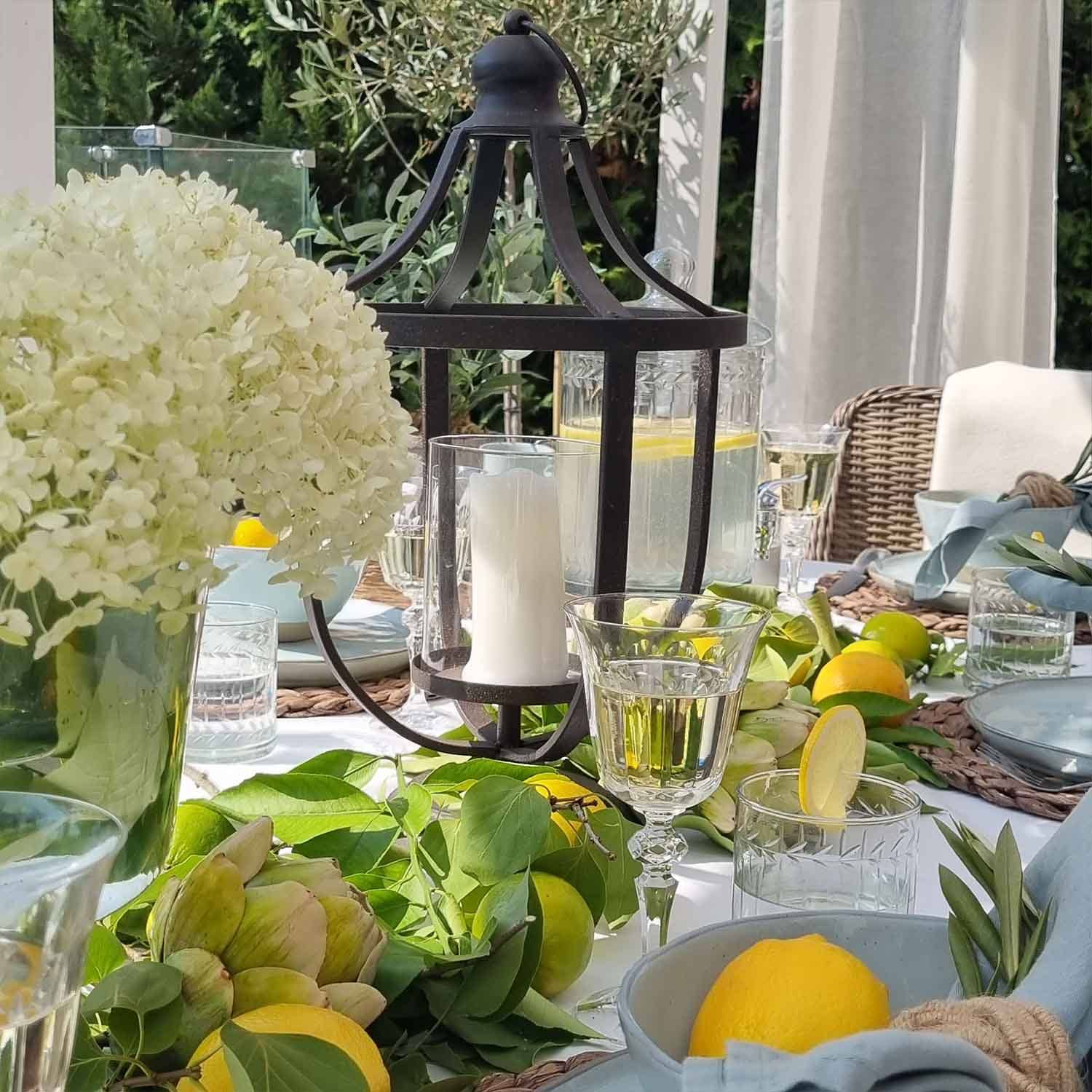 Schwarzer Metall-Lampion mit weisser Kerze auf sommerlich dekoriertem Tisch mit Zitronen und grünen Blättern