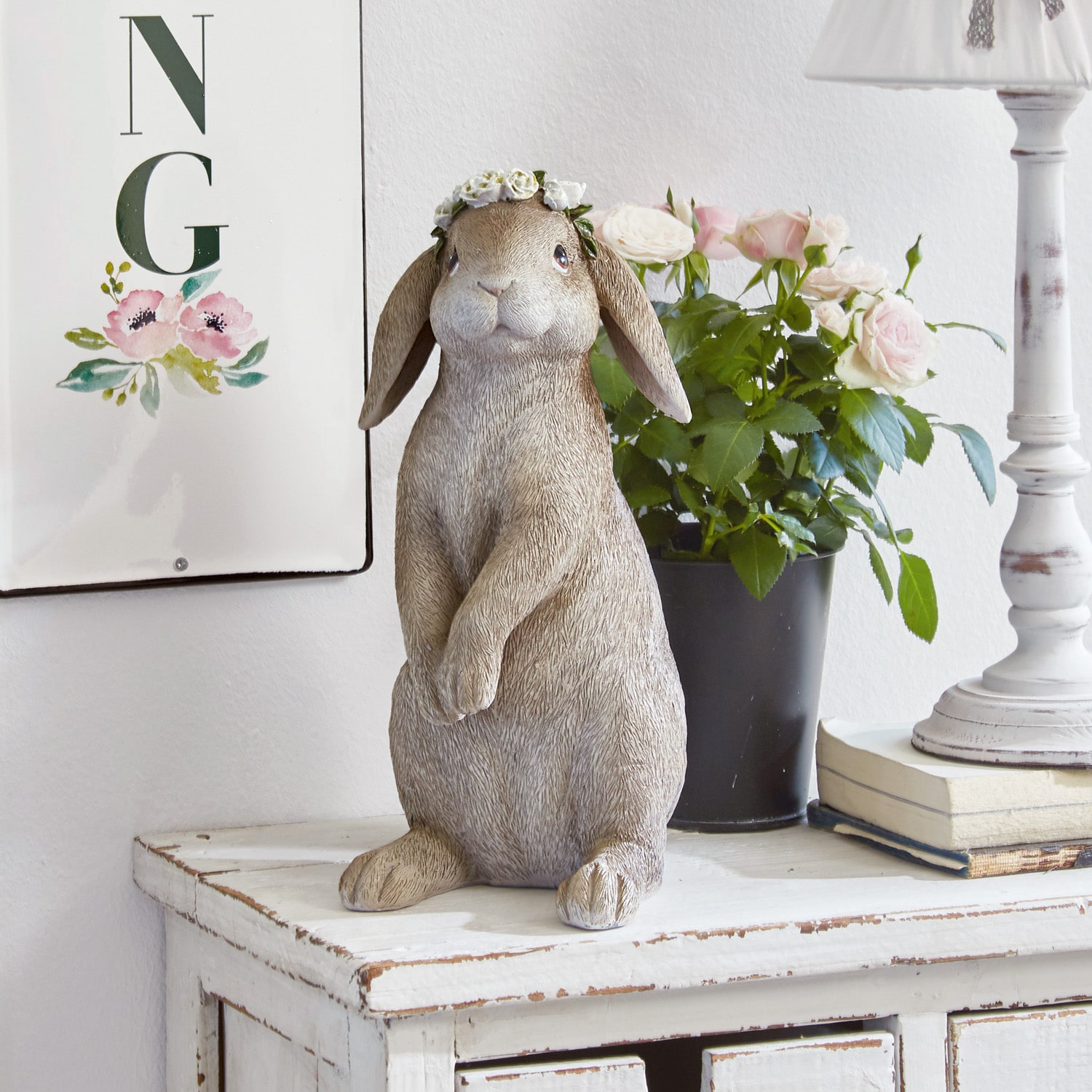 Dekorative Hasenfigur in Beige mit Blumenkranz auf weisser Holzkommode stehend