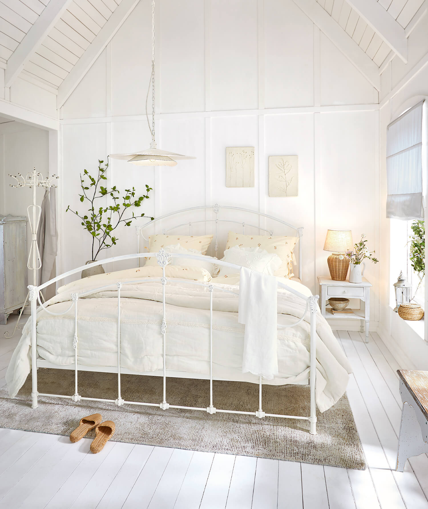 Weisses Metallbettgestell in hellem Schlafzimmer mit cremefarbiger Bettwäsche und Naturteppich